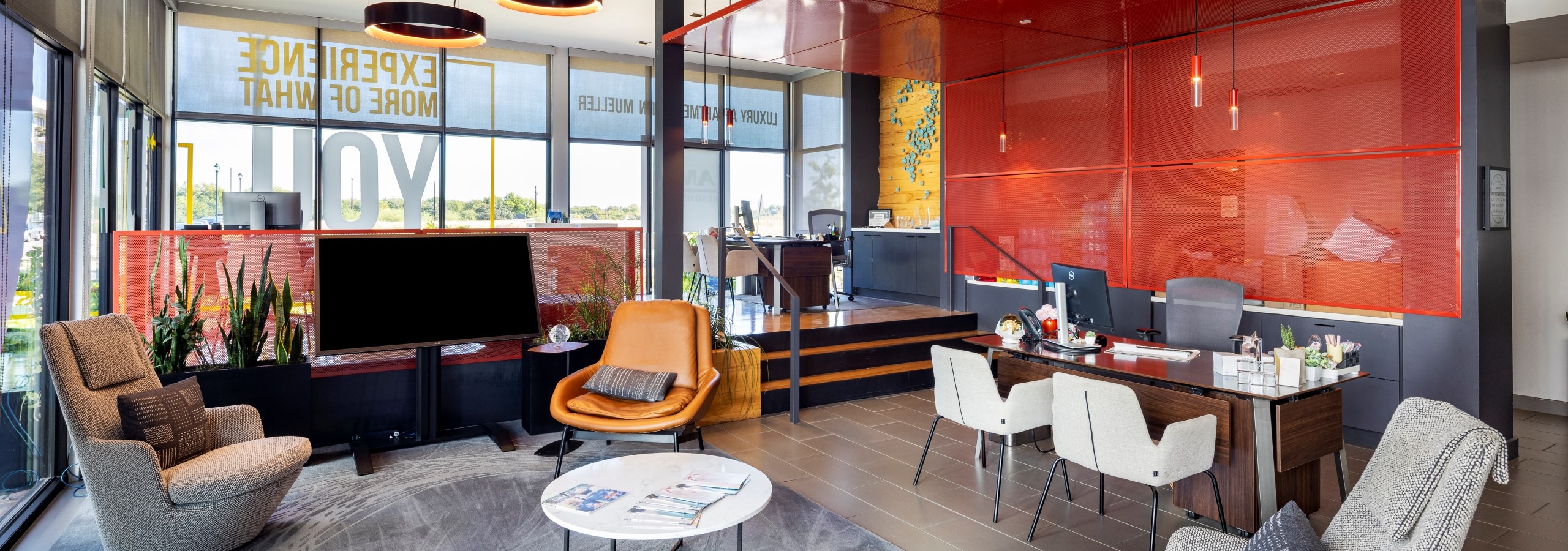 Leasing office at AMLI on Aldrich apartments with orange and gray décor, desks, comfortable chairs, and a flat screen TV and large windows.