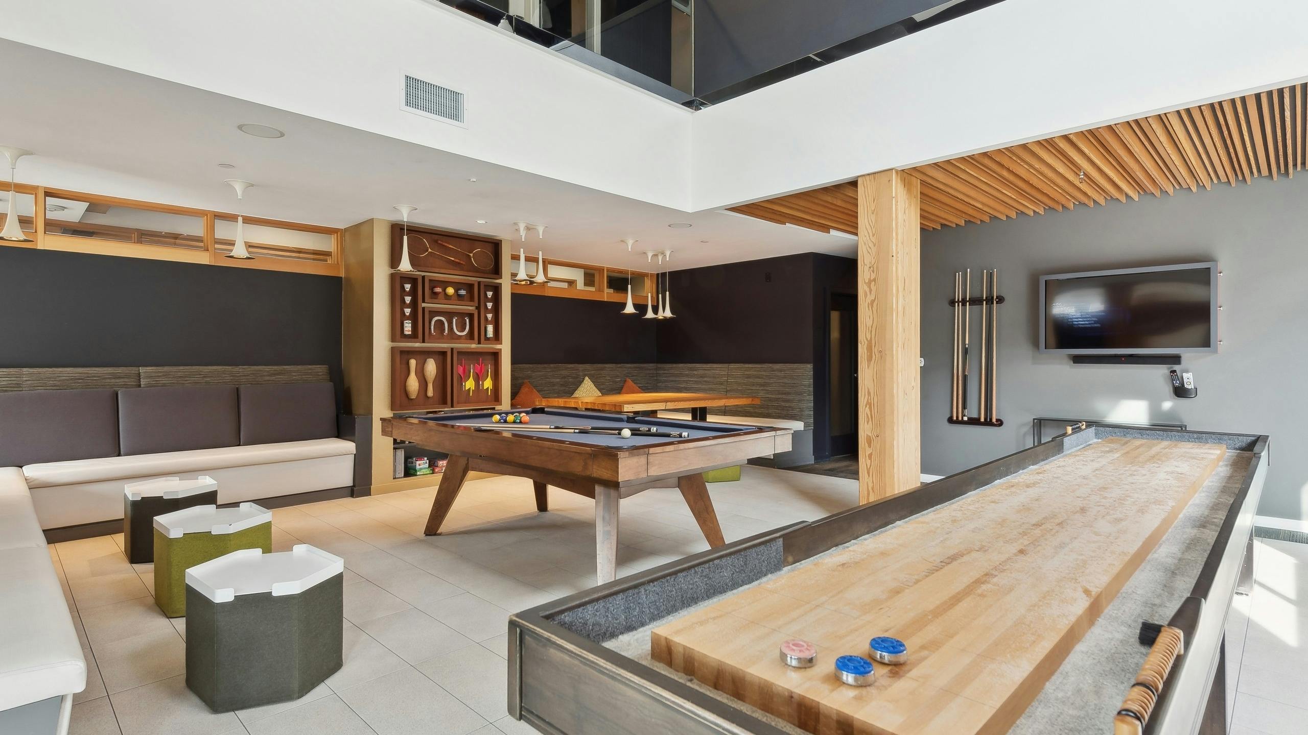 Resident game room at AMLI Wallingford apartments with a billiards table and shuffleboard with a board game shelf in the background.
