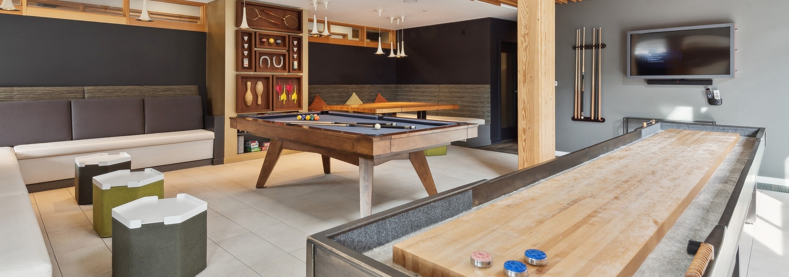 Resident game room at AMLI Wallingford apartments with a billiards table and shuffleboard with a board game shelf in the background.