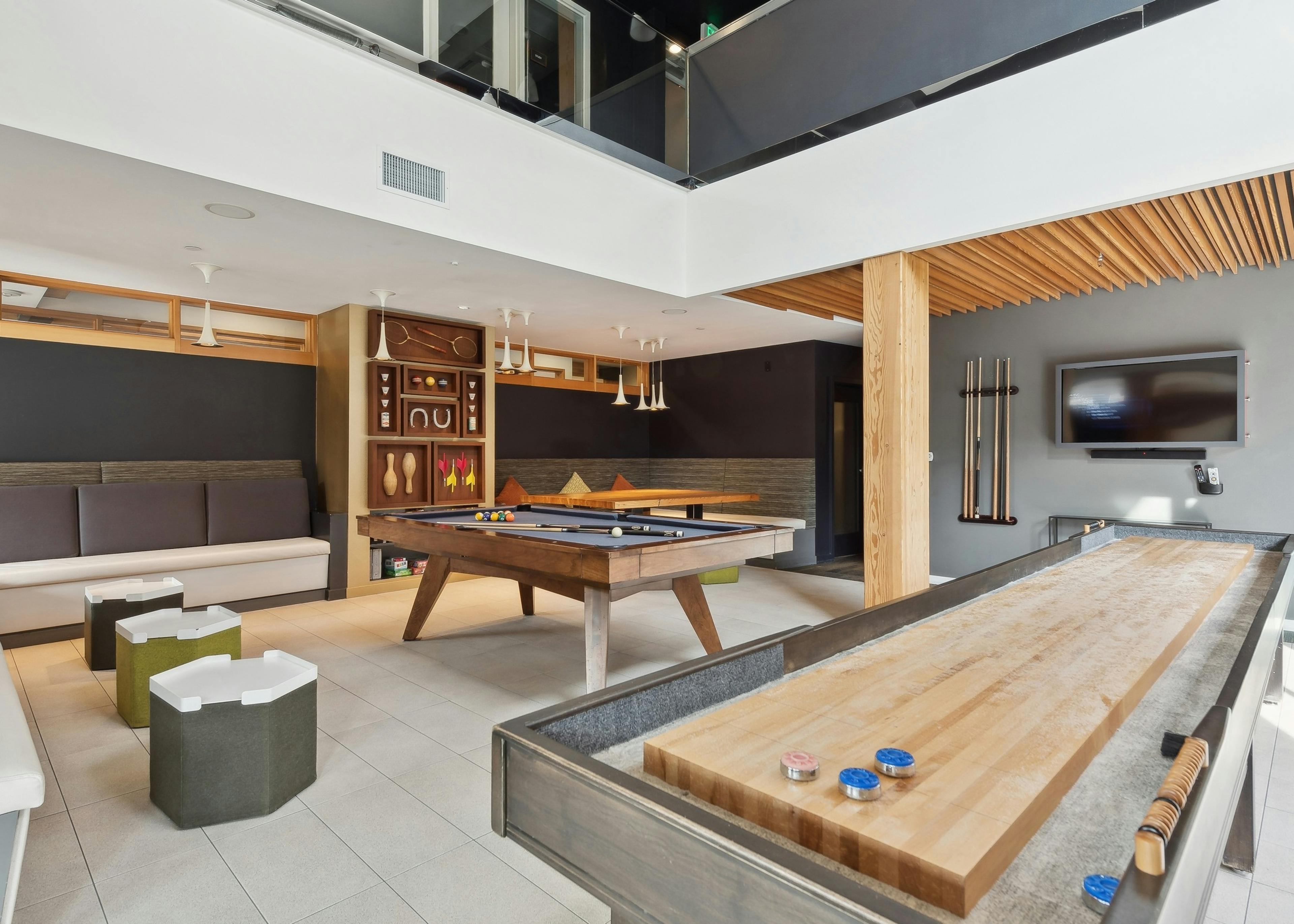 Resident game room at AMLI Wallingford apartments with a billiards table and shuffleboard with a board game shelf in the background.