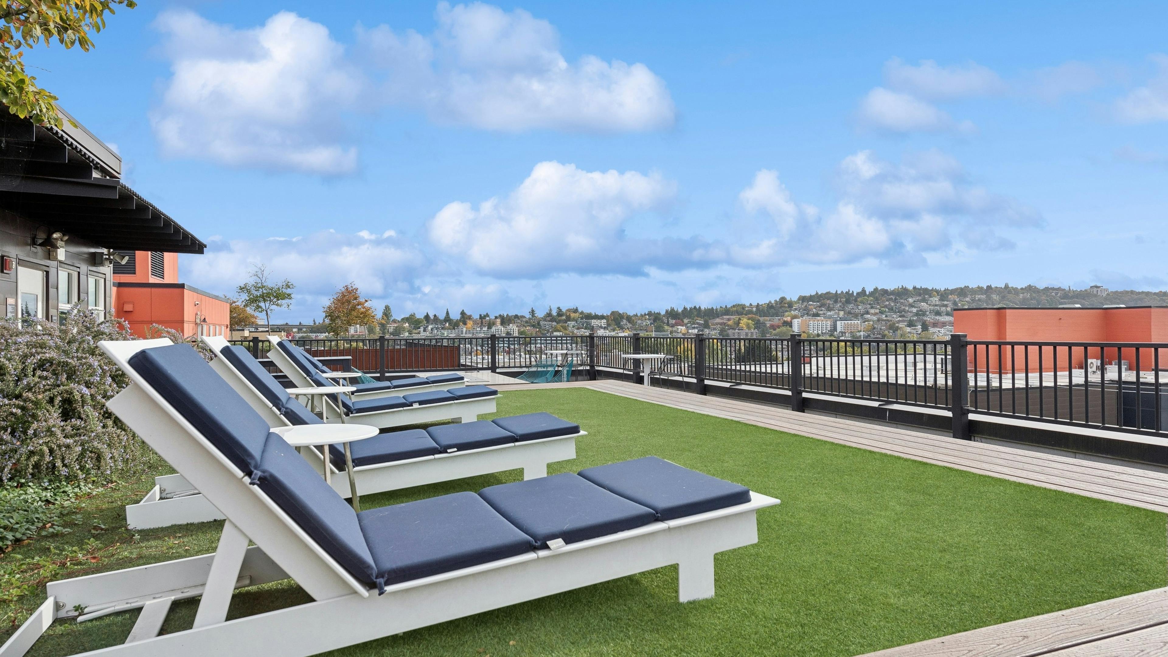 AMLI Wallingford rooftop featuring multiple lounge chairs on green turf and sweeping views of Seattle skyline and surrounding neighborhoods.
