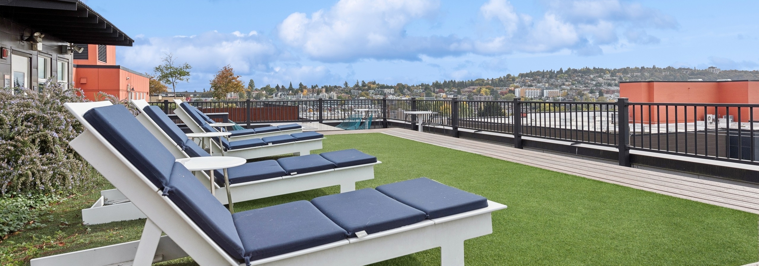 AMLI Wallingford rooftop featuring multiple lounge chairs on green turf and sweeping views of Seattle skyline and surrounding neighborhoods.