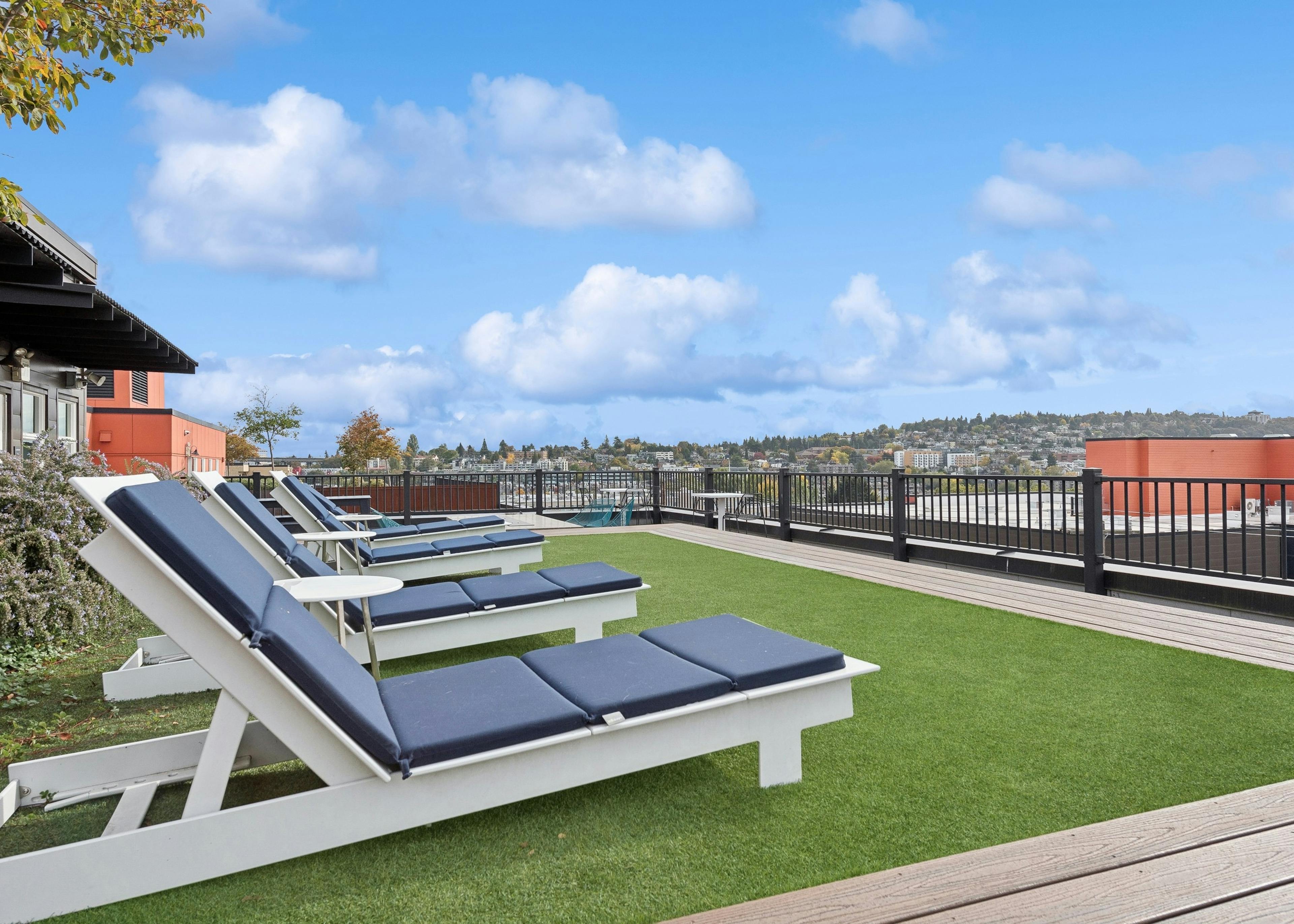AMLI Wallingford rooftop featuring multiple lounge chairs on green turf and sweeping views of Seattle skyline and surrounding neighborhoods.