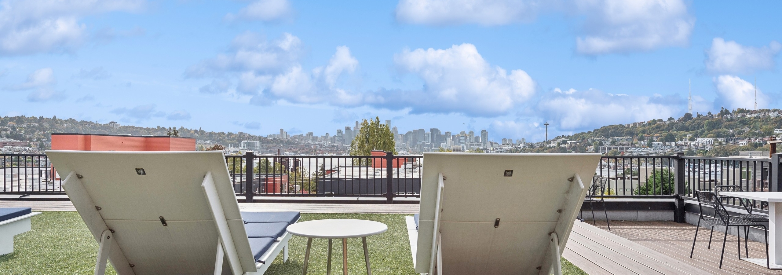 Daytime view of AMLI Wallingford apartment rooftop showcasing two lounge chairs facing the views of the Seattle skyline and Lake Union.
