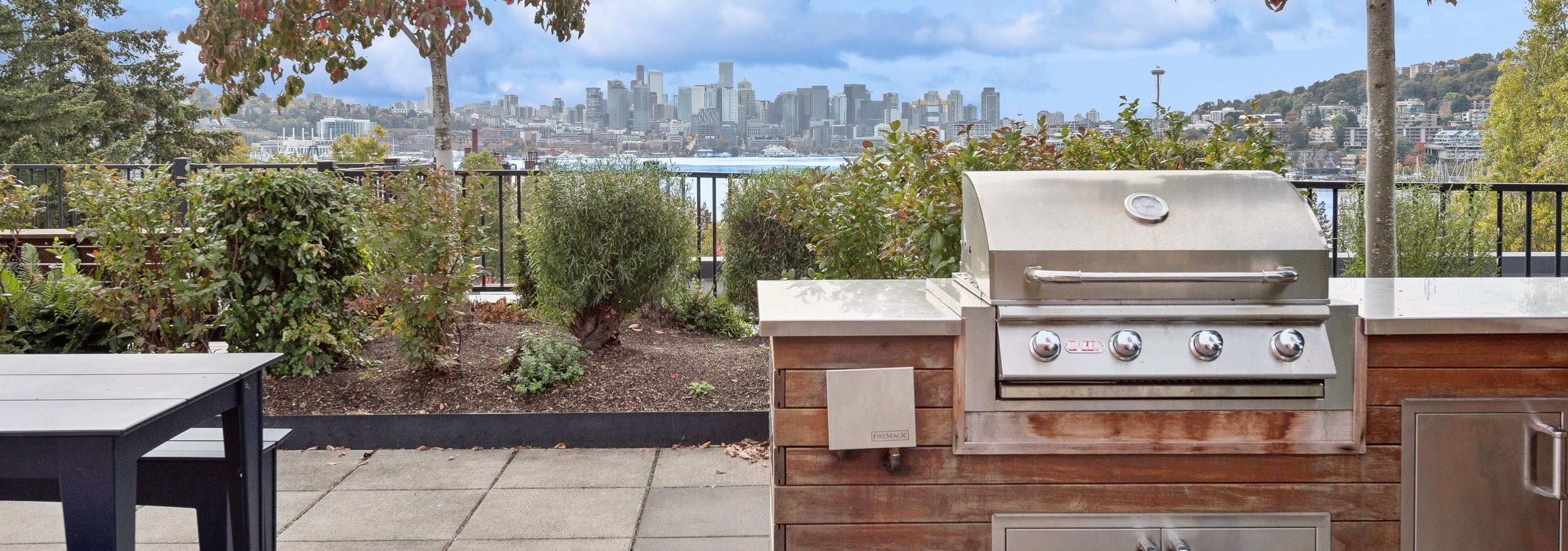Daytime view of AMLI Wallingford apartment rooftop with a stainless grill in the foreground and views of Seattle skyline and Lake Union