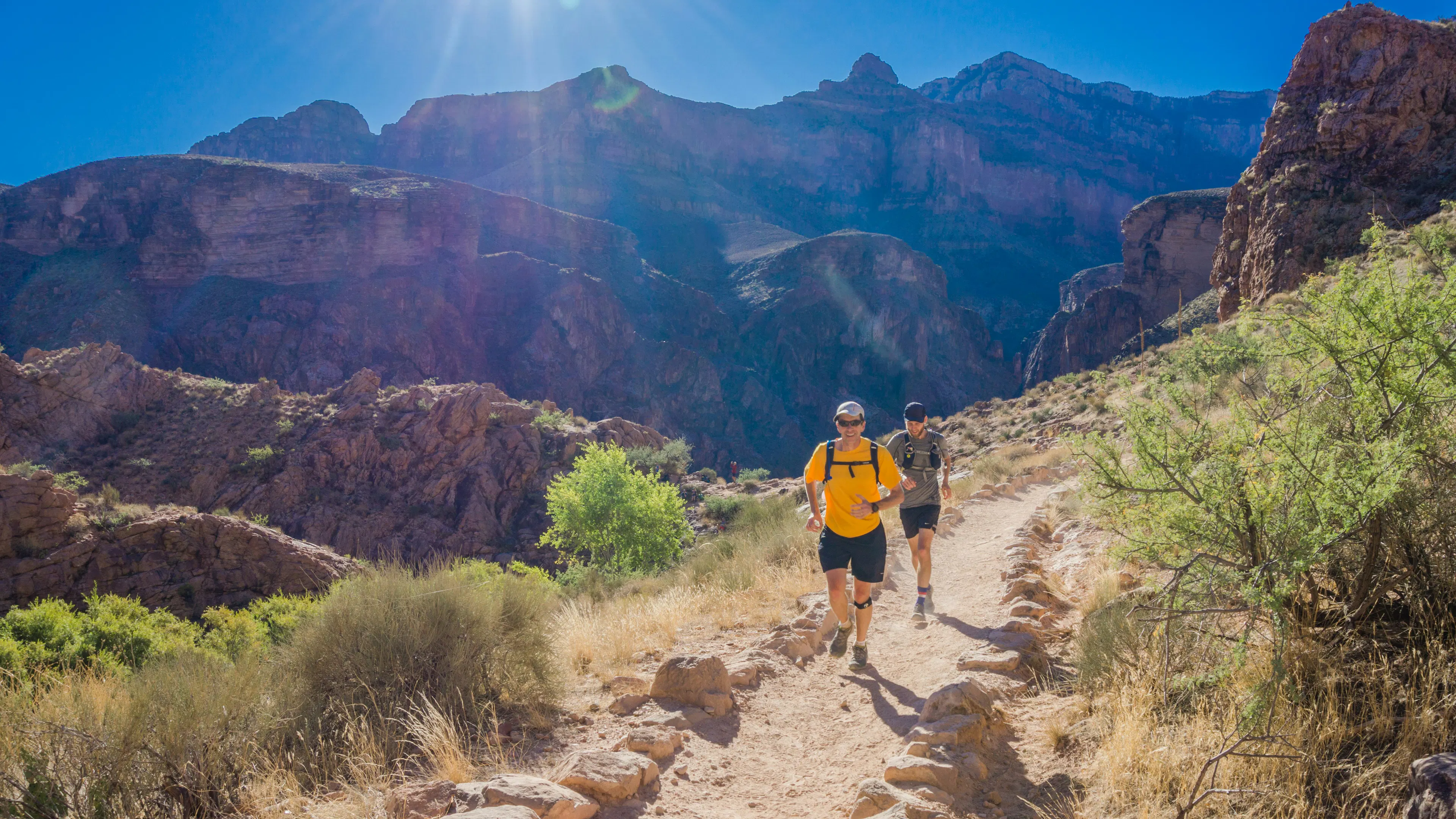 Two runners running up a steep hill on the side of a canyon cliff