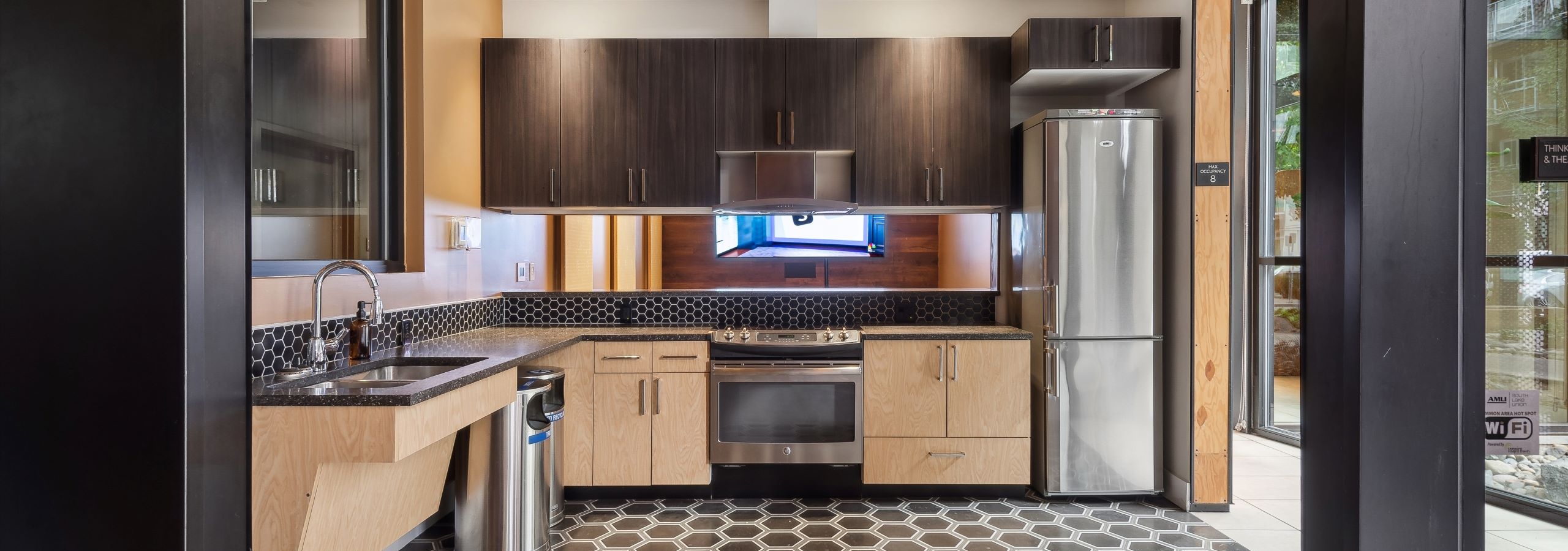 Resident kitchen at AMLI South Lake Union featuring wooden cabinets with tile backsplash and stainless steel appliances