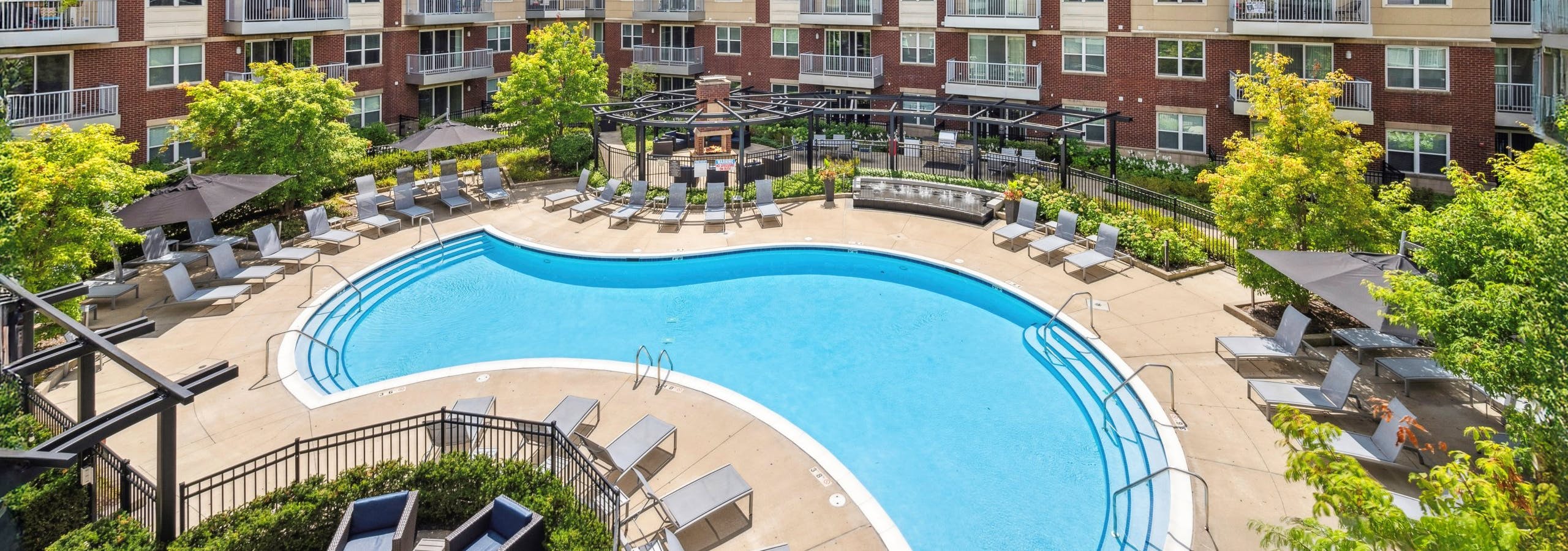 Elevated view of pool courtyard with lounge chairs, trees and balconies under a blue sky at AMLI Deerfield apartments.