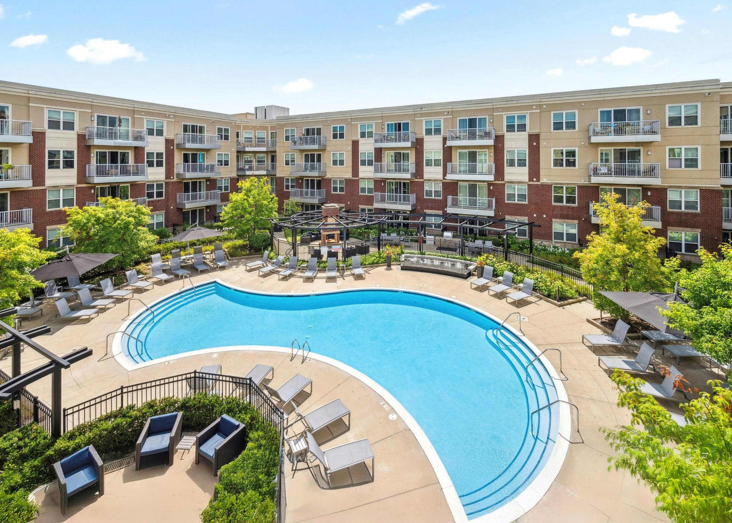 Elevated view of pool courtyard with lounge chairs, trees and balconies under a blue sky at AMLI Deerfield apartments.