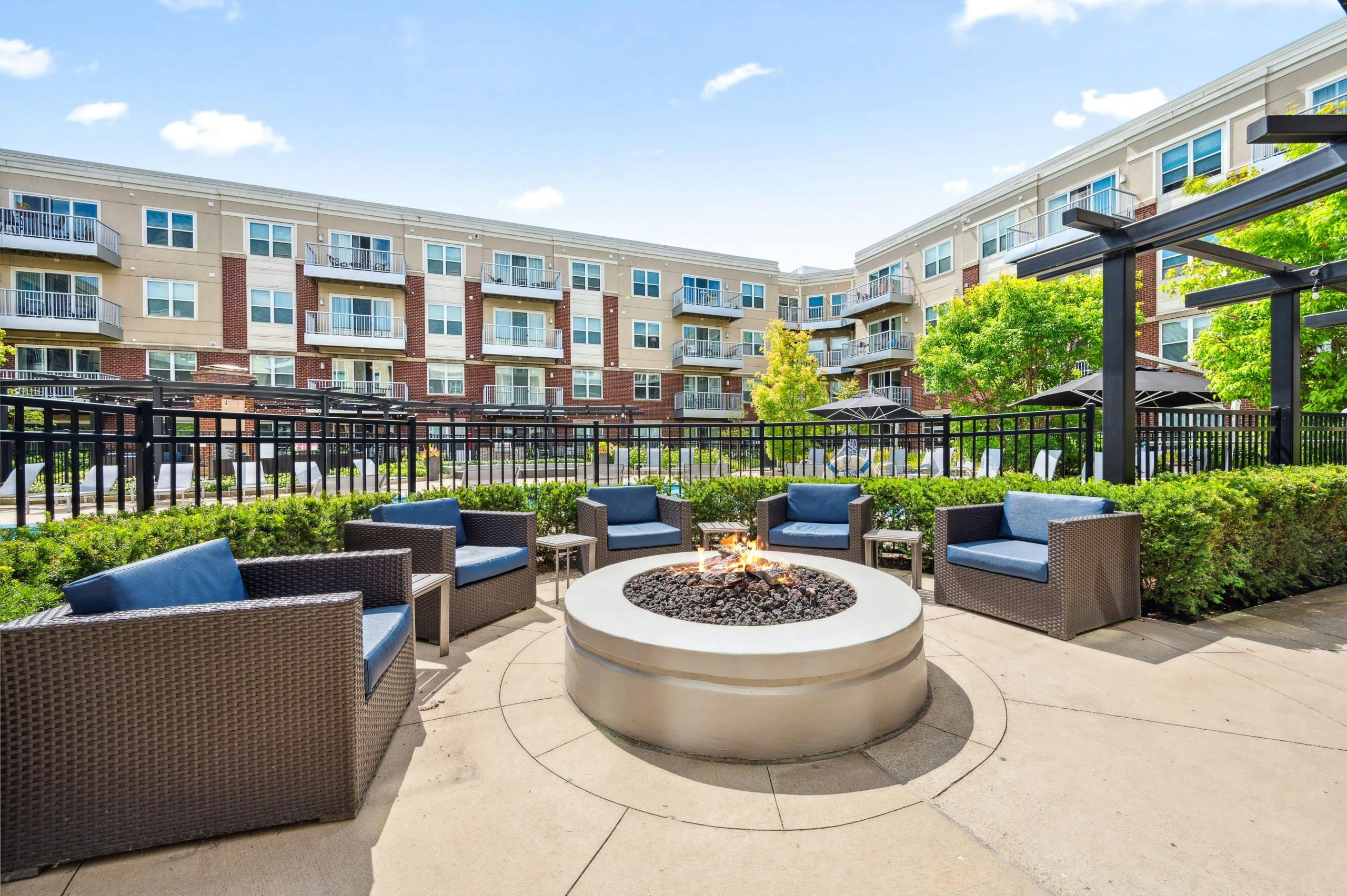 Exterior view of fire pit lounge area surrounded by wicker chairs in front of pool gate with apartments in background at AMLI Deerfield.