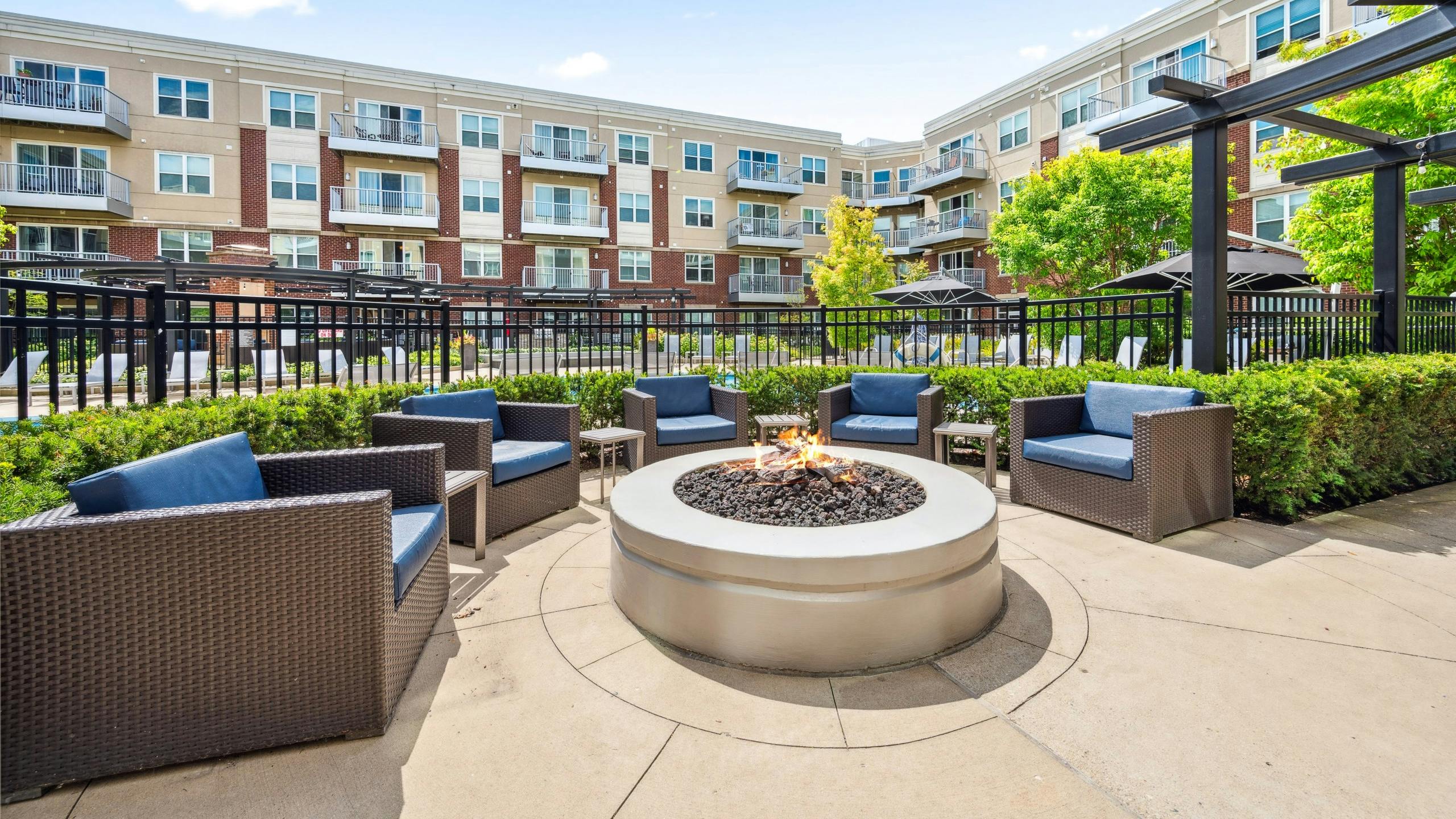 Exterior view of fire pit lounge area surrounded by wicker chairs in front of pool gate with apartments in background at AMLI Deerfield.