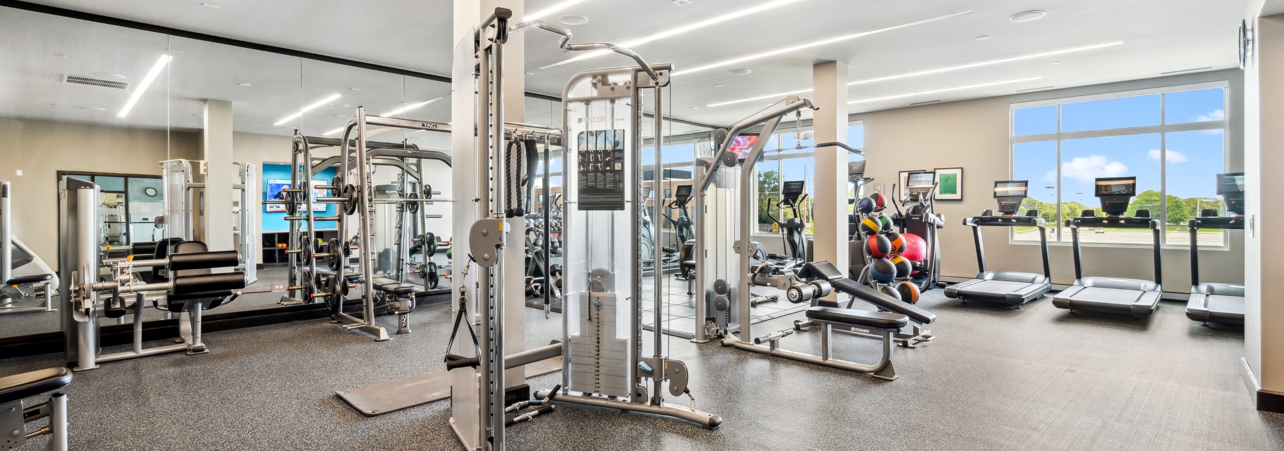 Expansive fitness center at AMLI Deerfield apartment building with treadmills, weight machines and large mirrors and wall of windows.