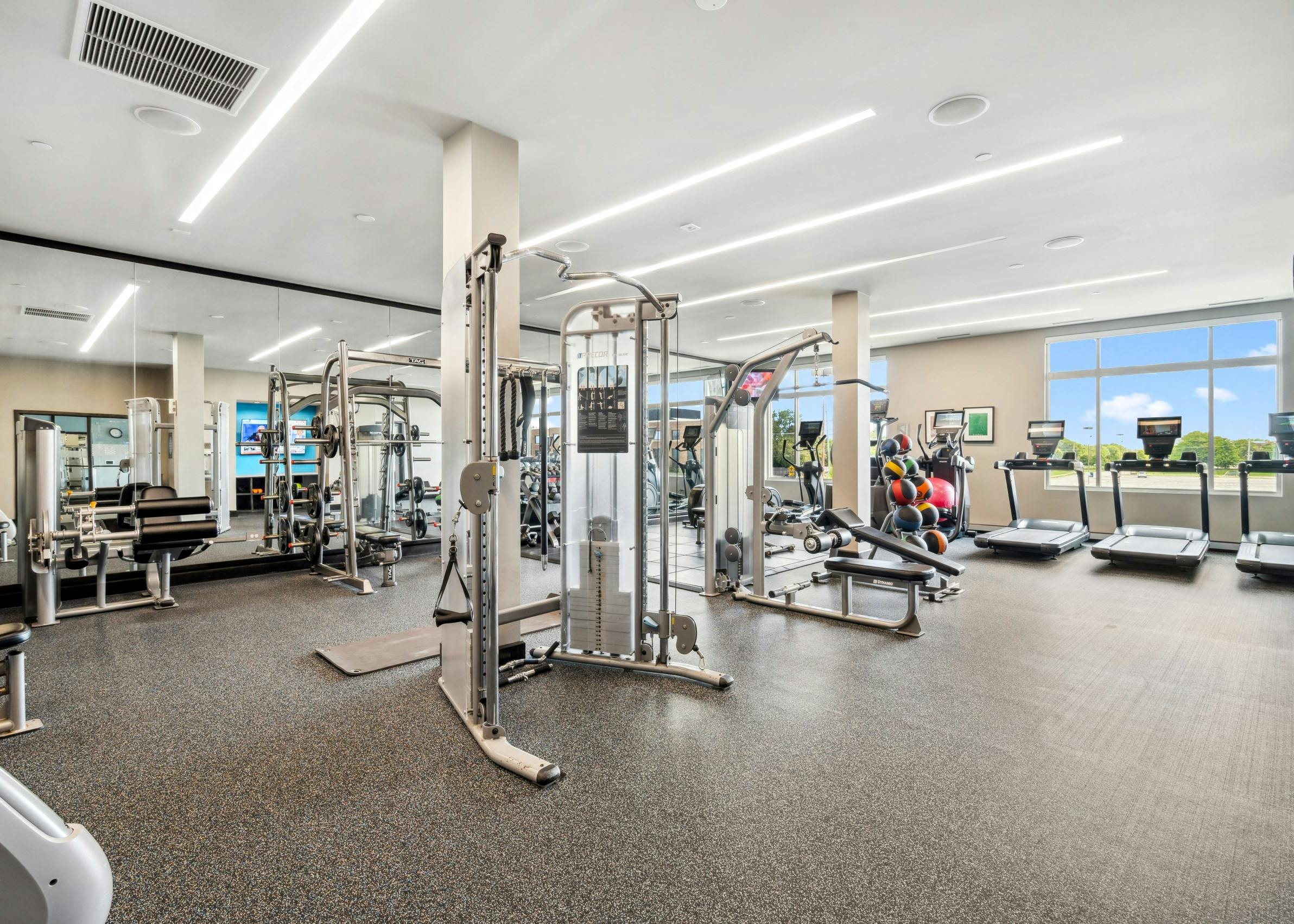 Large fitness center at AMLI Deerfield apartment building with treadmills, weight machines and large mirrors and wall of windows.