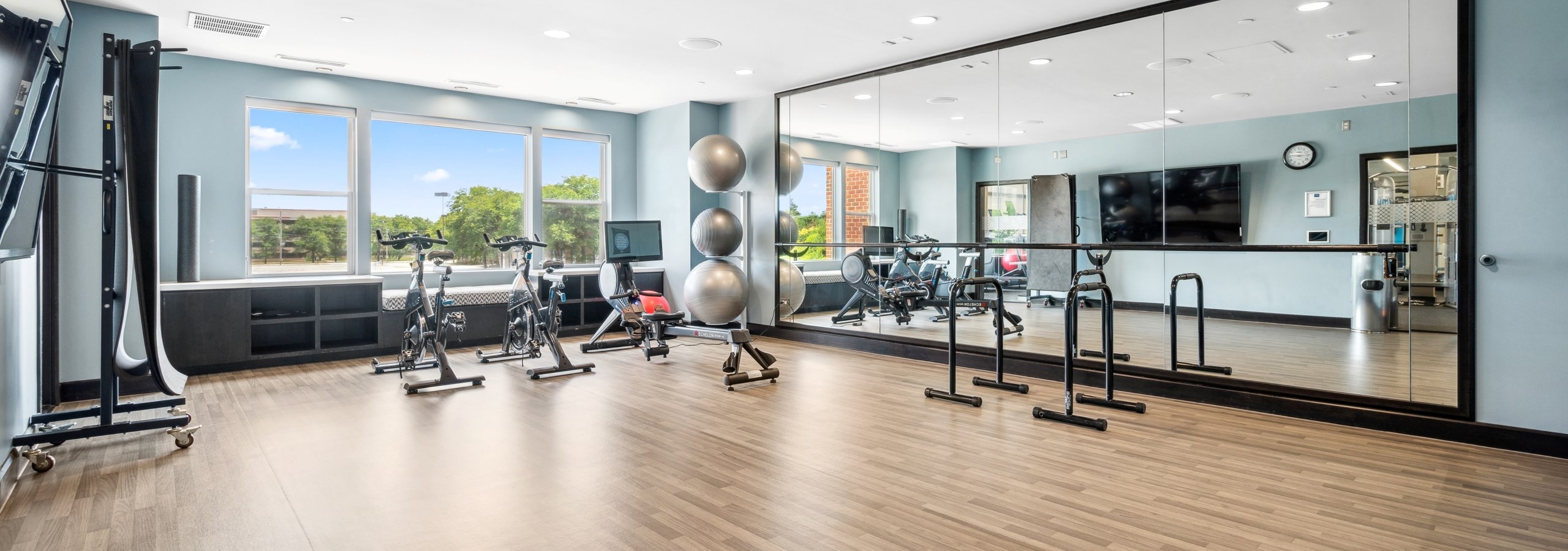 Interior view of AMLI Deerfield yoga room with spin bikes, mirrored wall, TV, large windows and wood floor.
