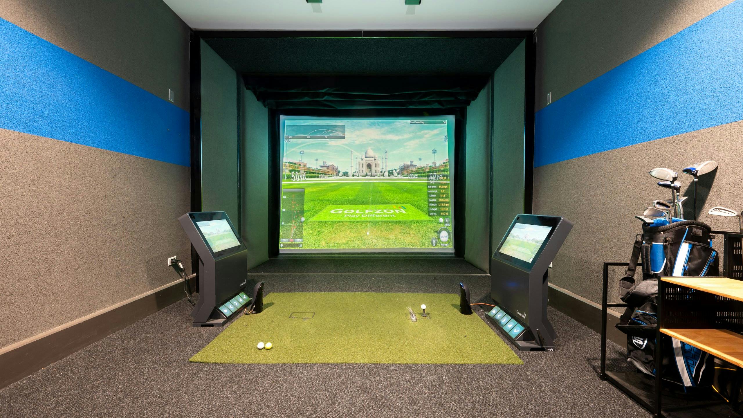 Indoor golf simulator at AMLI Deerfield with simulated course image on large screen, golf equipment and smaller navigation screens