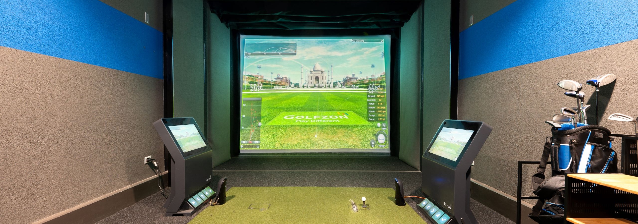 Indoor golf simulator at AMLI Deerfield with simulated course image on large screen, golf equipment and smaller navigation screens