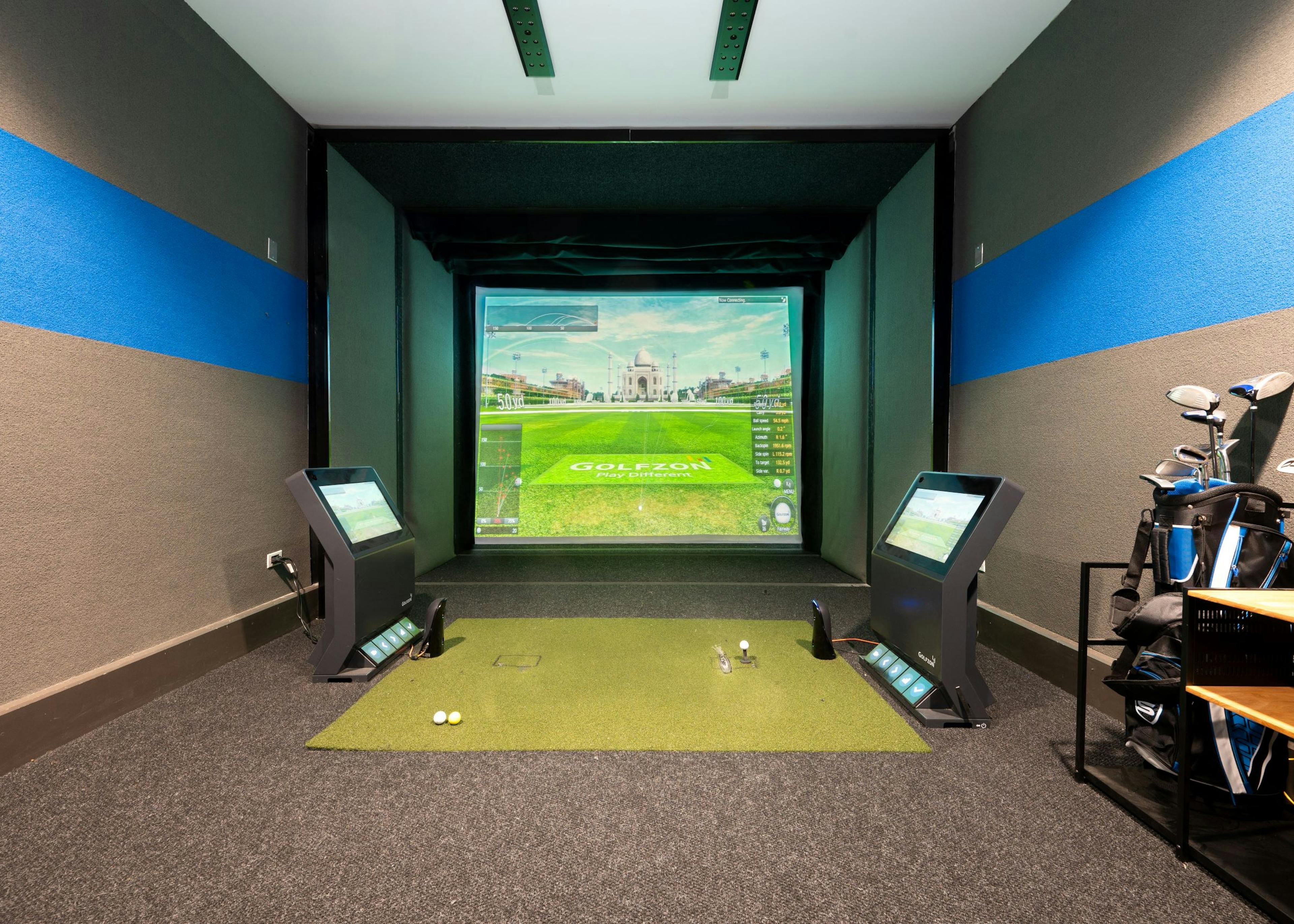 Indoor golf simulator at AMLI Deerfield with simulated course image on large screen, golf equipment and smaller navigation screens 
