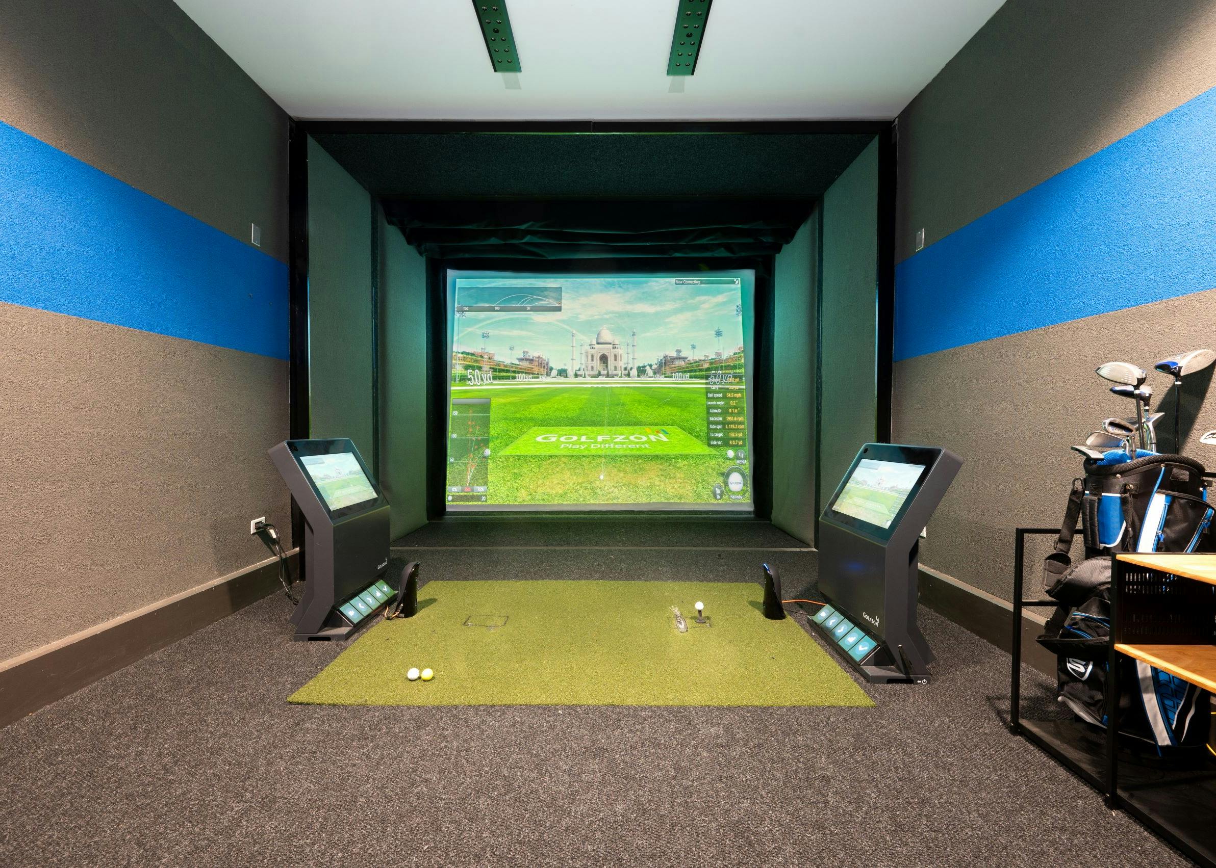 Indoor golf simulator at AMLI Deerfield with simulated course image on large screen, golf equipment and smaller navigation screens