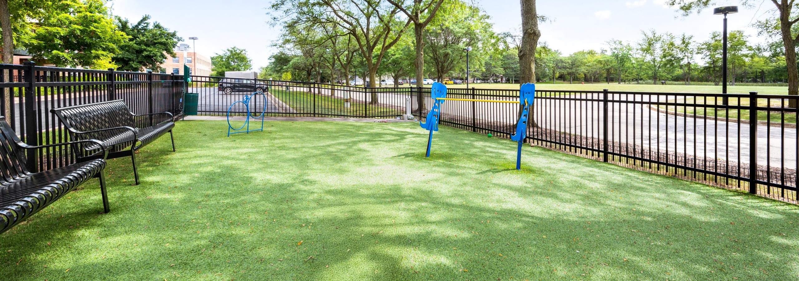 AMLI Deerfield fenced in dog park with benches and blue agility equipment set on grass and surrounded by trees