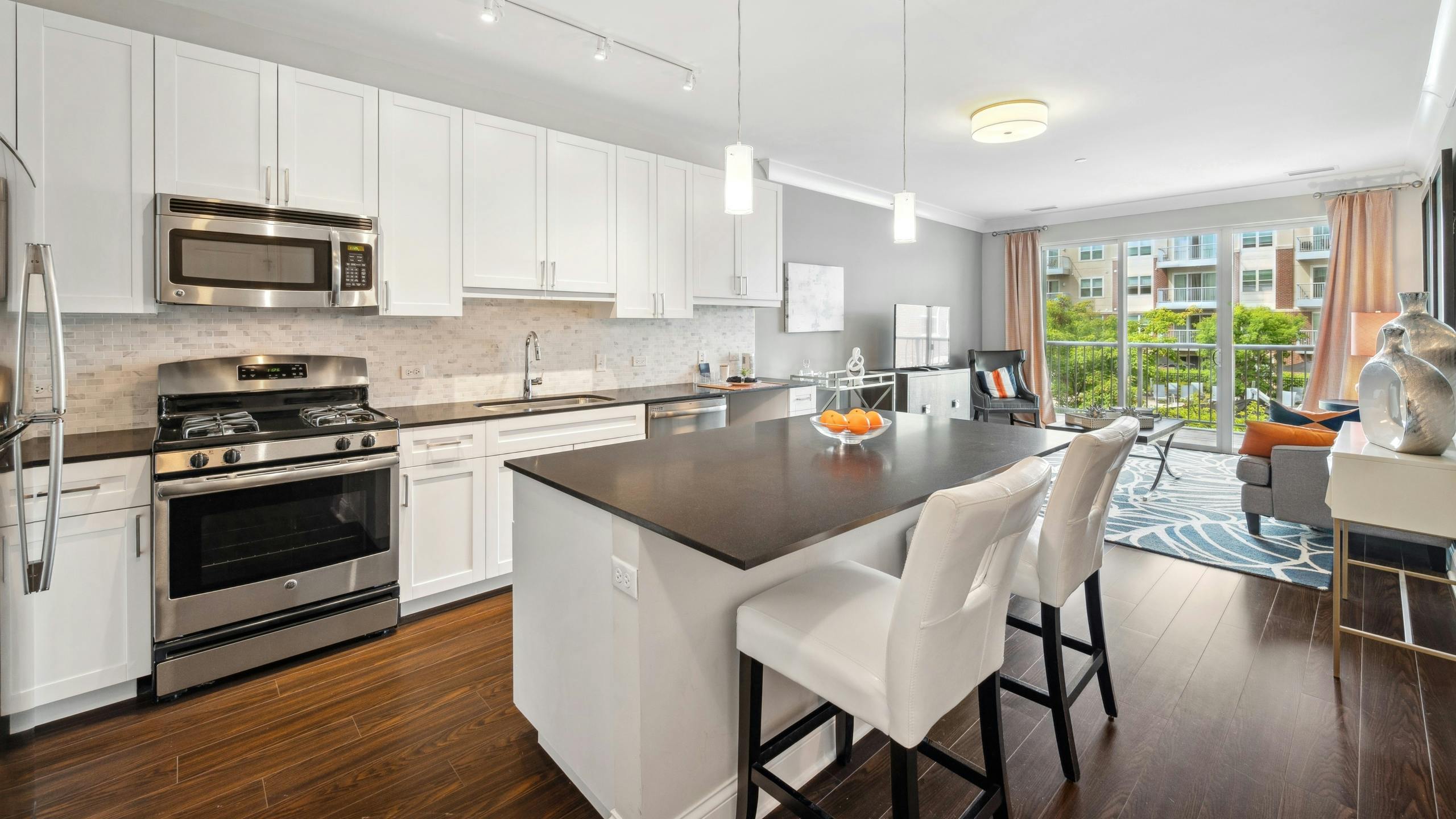 Interior view of AMLI Deerfield kitchen with white cabinets, stainless steel appliances, and large island opening up to living room.