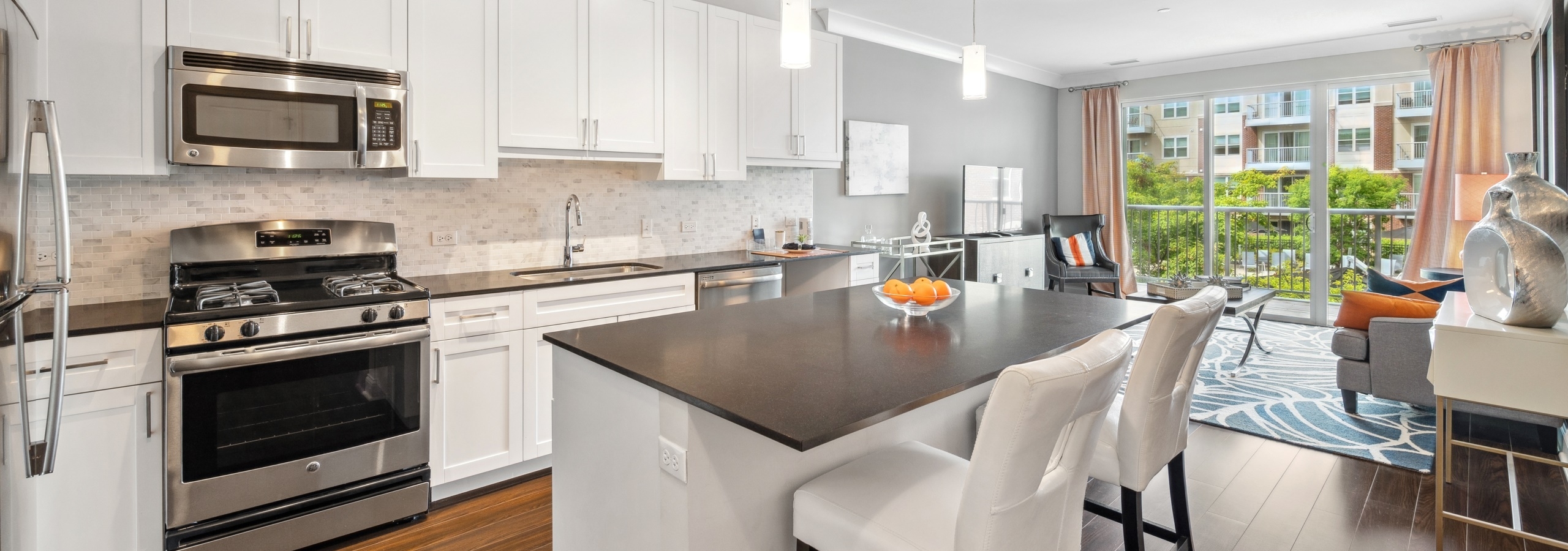 Interior view of AMLI Deerfield kitchen with white cabinets, stainless steel appliances, and large island opening up to living room.