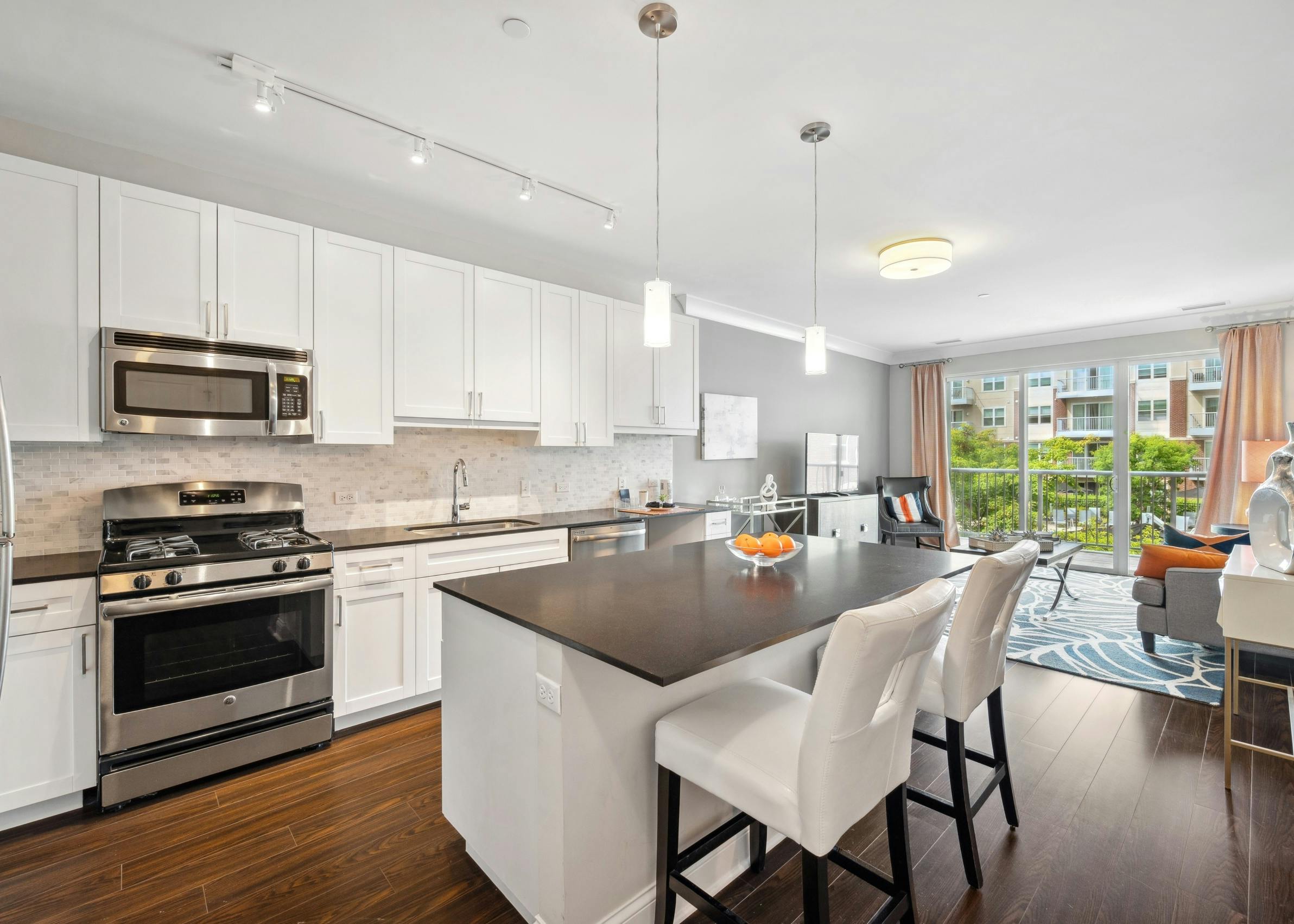 Interior view of AMLI Deerfield kitchen with white cabinets, stainless steel appliances, and large island opening up to living room.