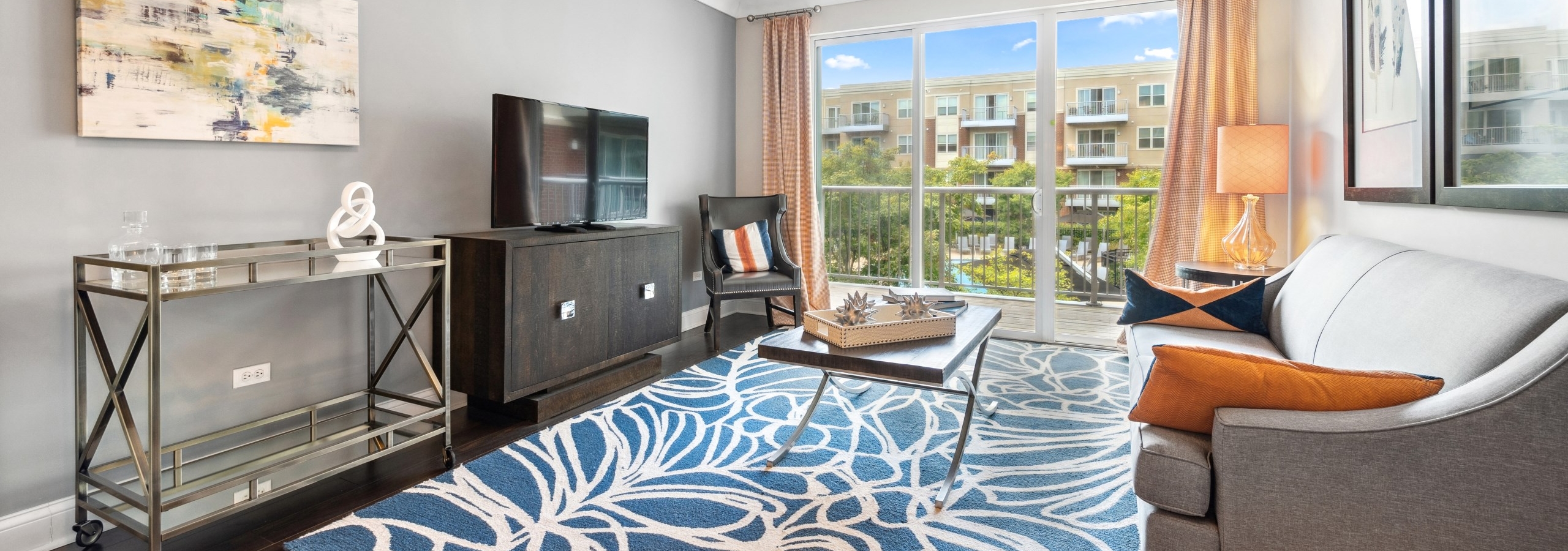 AMLI Deerfield living room with modern furniture, blue patterned area rug and sliding glass doors opening up to a balcony view.