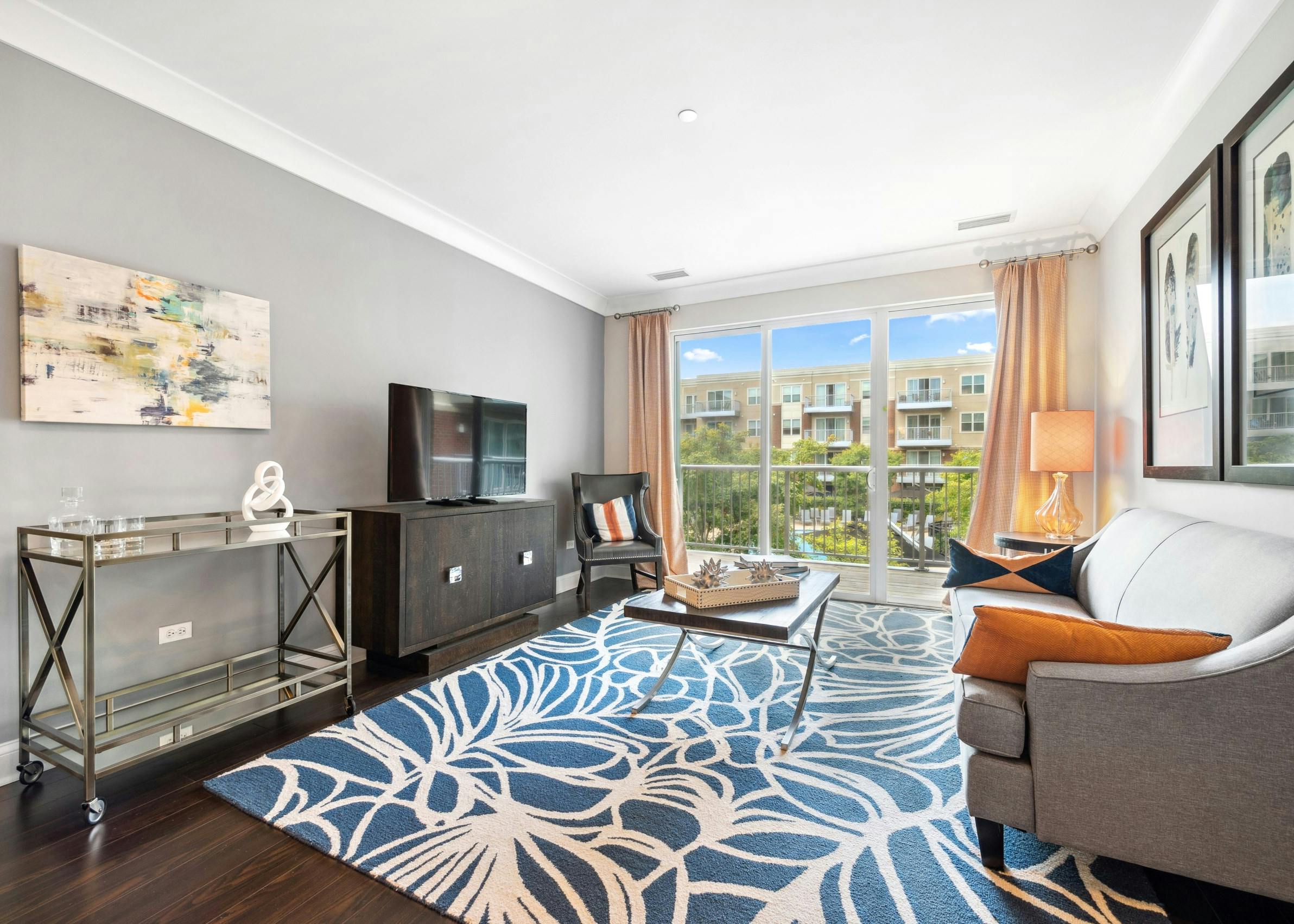 AMLI Deerfield living room with modern furniture, blue patterned area rug and sliding glass doors opening up to a balcony view.
