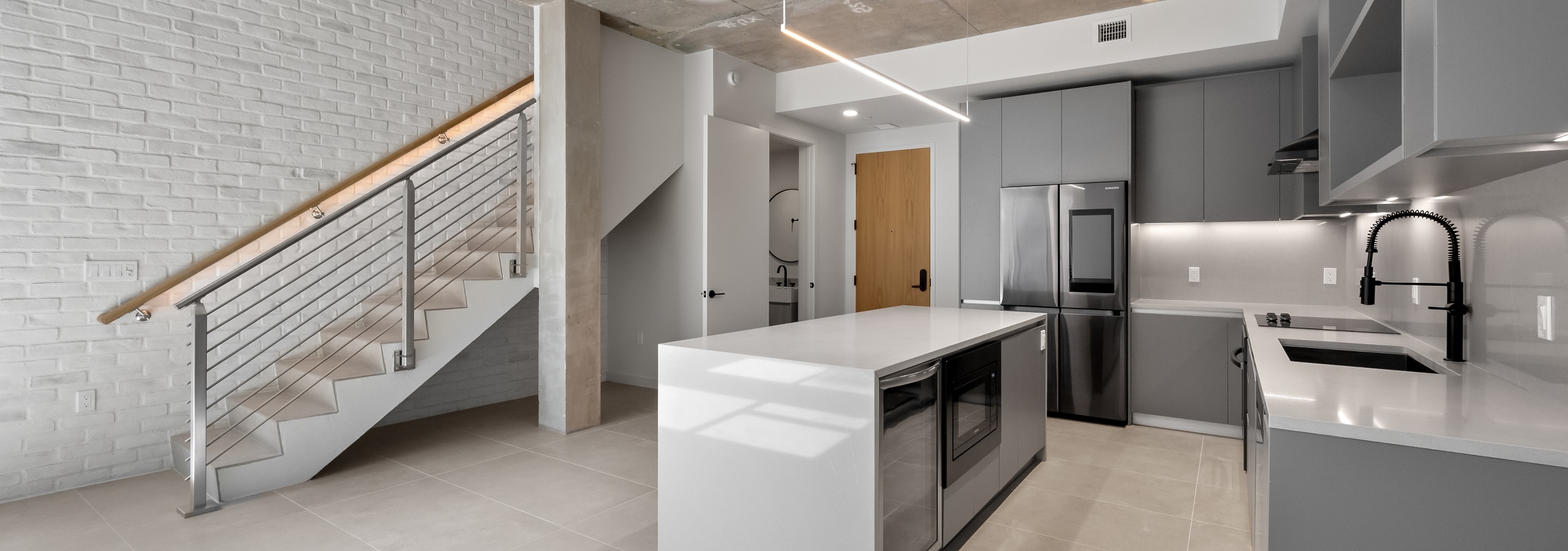 Modern island kitchen with stainless steel appliances, and gray modern cabinets adjacent to stairway to loft at AMLI Wynwood apartments.
