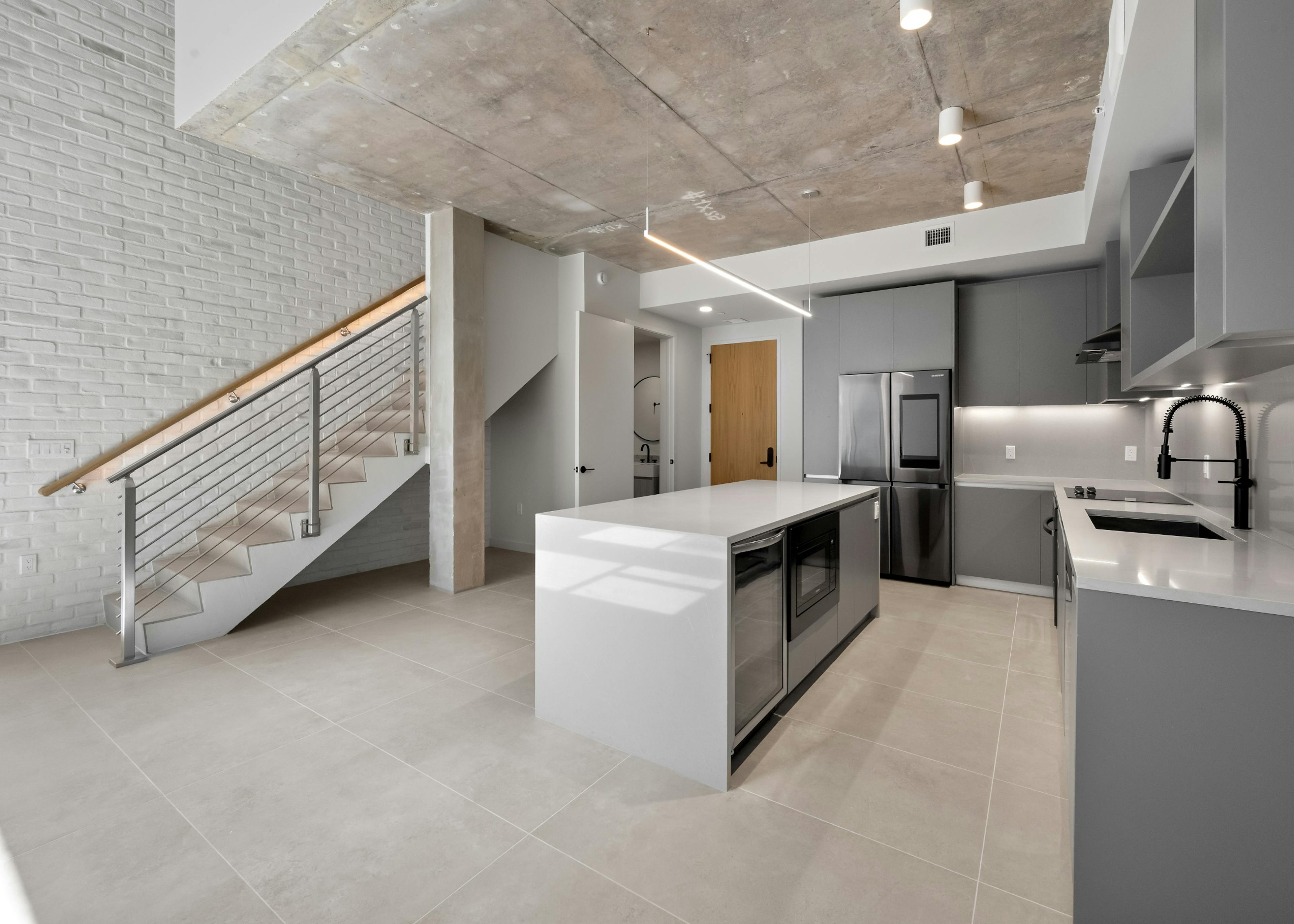 Modern island kitchen with stainless steel appliances, and gray modern cabinets adjacent to stairway to loft at AMLI Wynwood apartments.