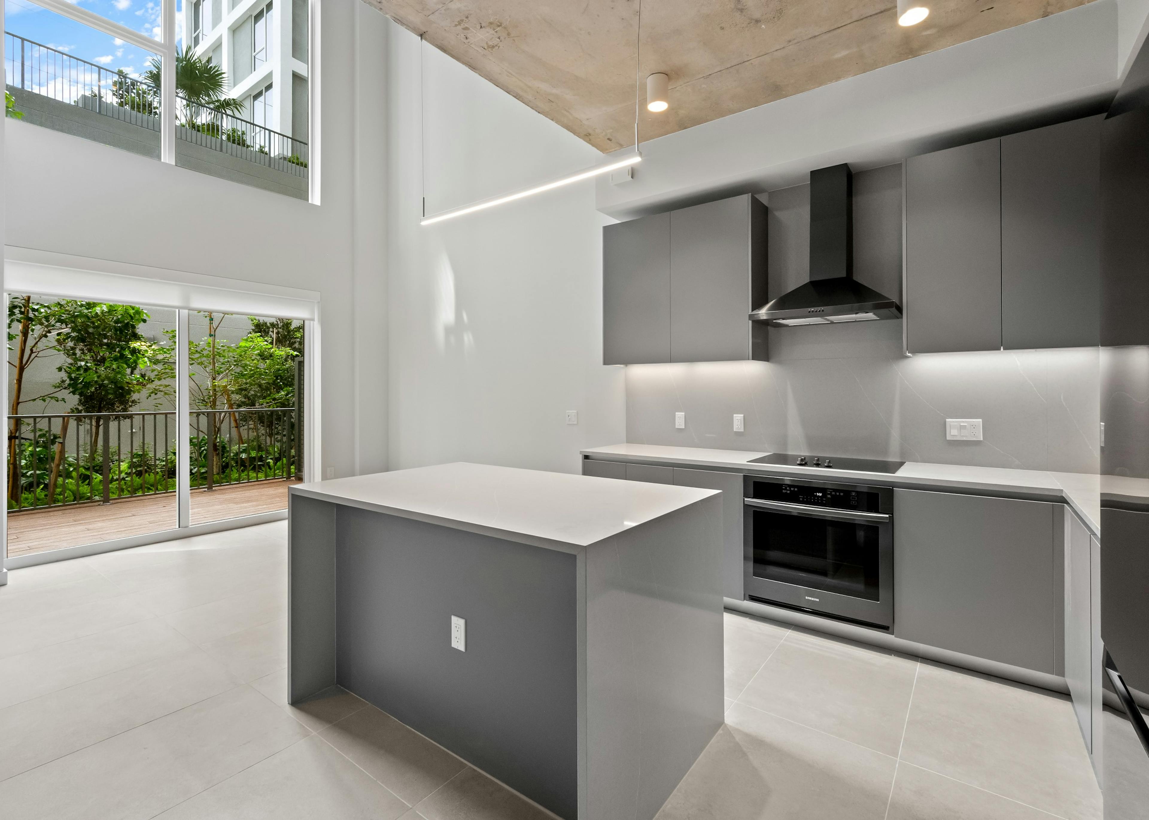 Interior view of modern kitchen and two-story living space with large windows and private patio at AMLI Wynwood apartments.