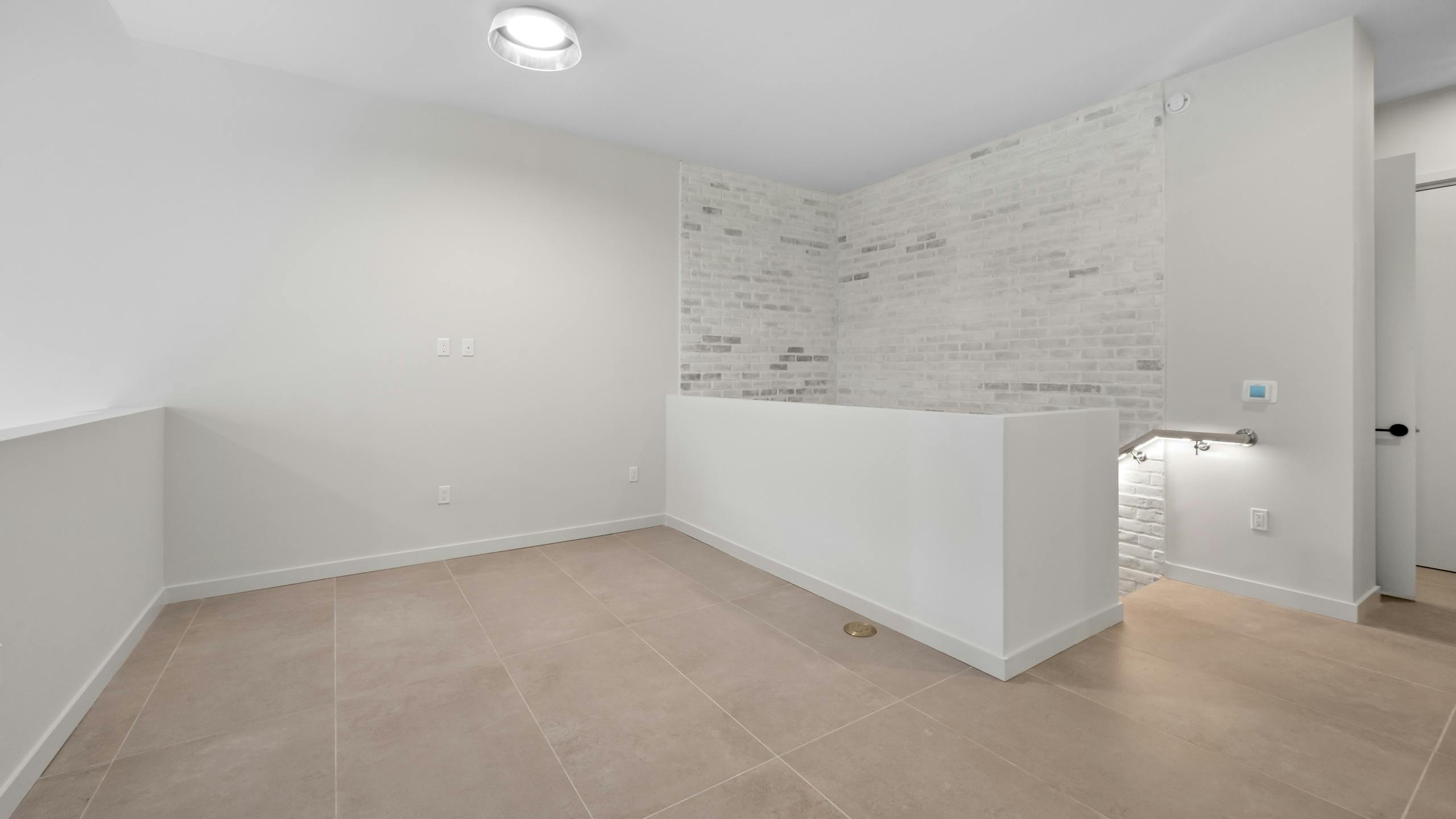 AMLI Wynwood open apartment living or working loft space with tan porcelain tiled flooring and white brick accent wall.