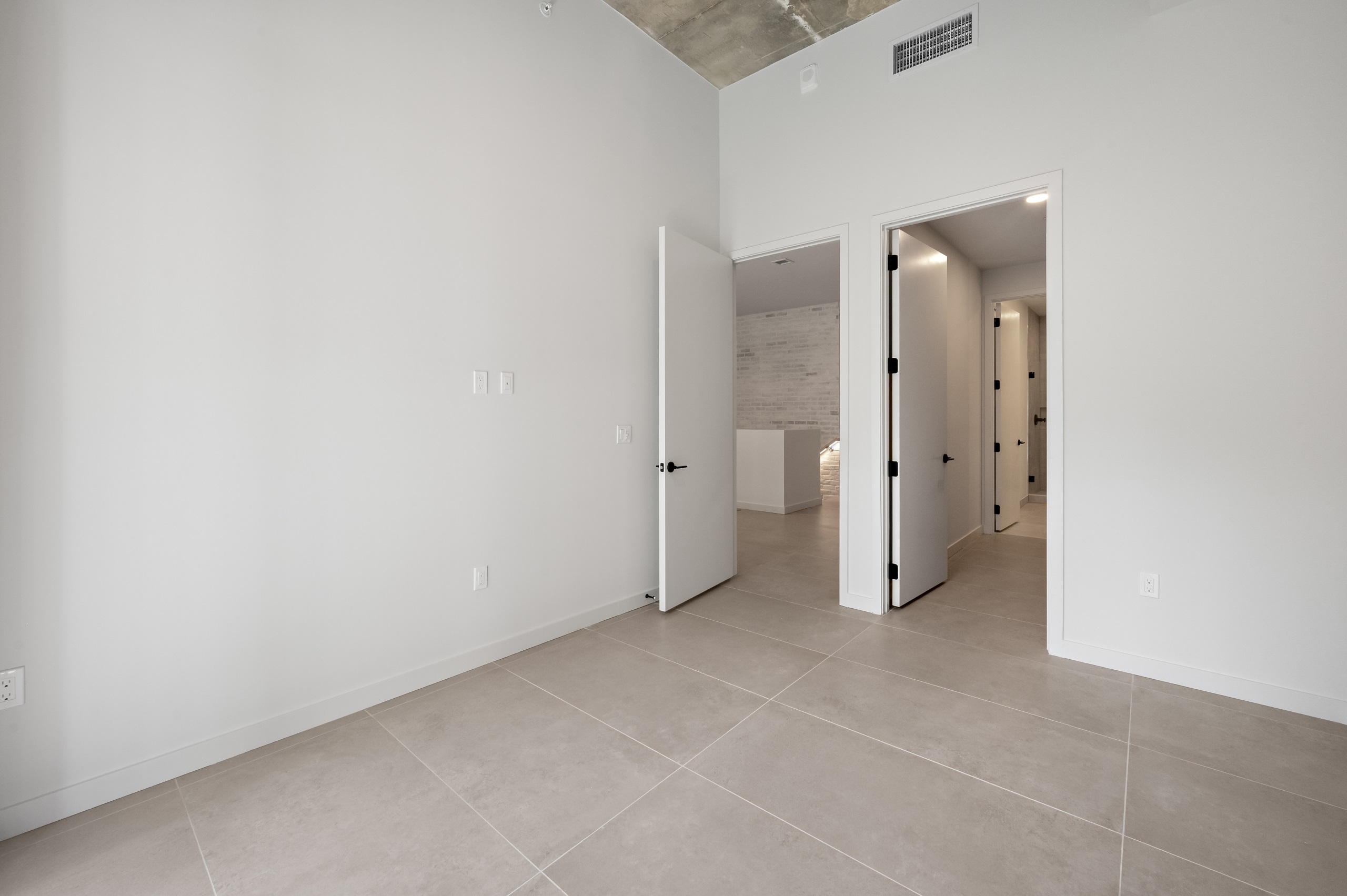 Interior view of large bedroom with tiled porcelain flooring, doors to living area and bathroom and white walls at AMLI Wynwood apartments.