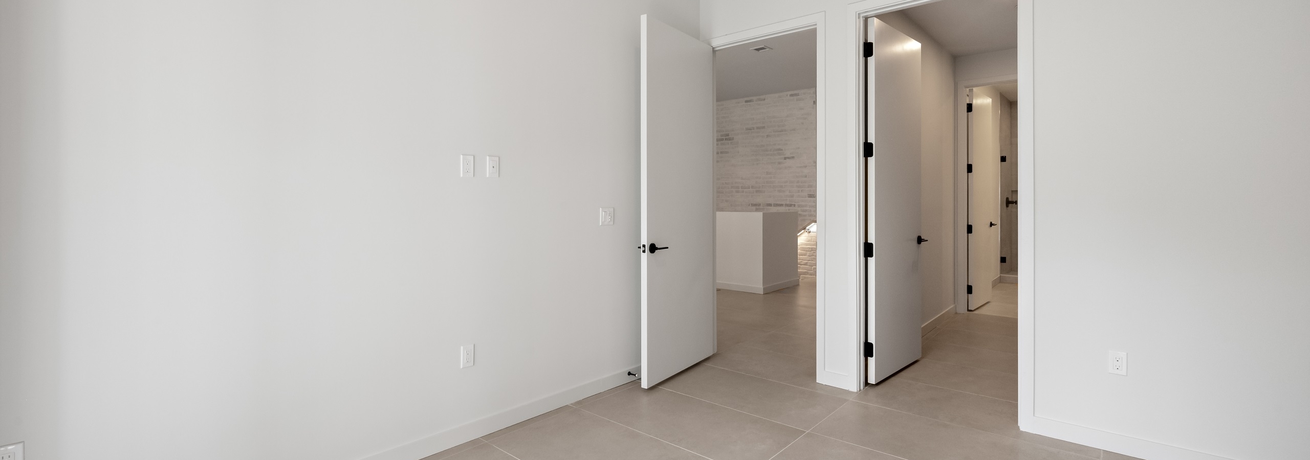 Interior view of large bedroom with tiled porcelain flooring, doors to living area and bathroom and white walls at AMLI Wynwood apartments.