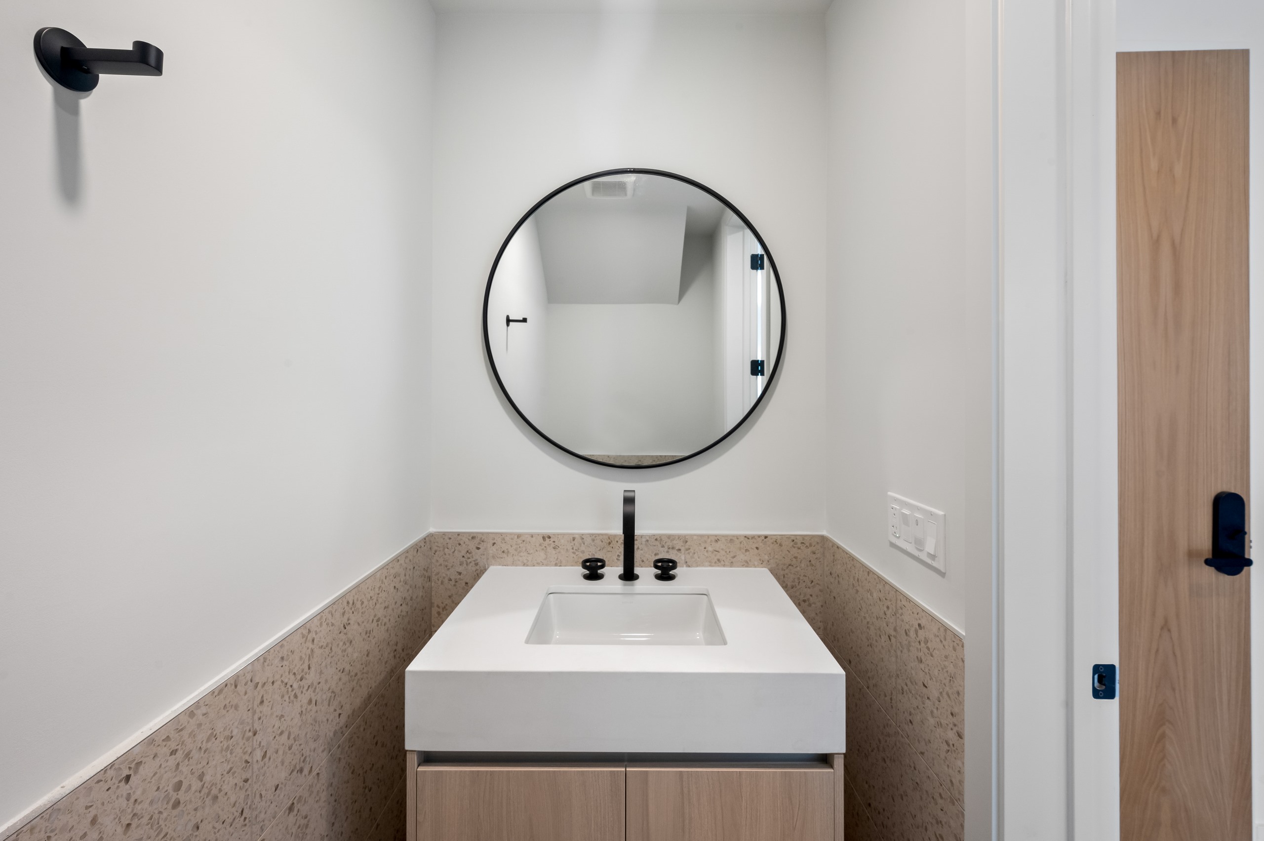 AMLI Wynwood powder room with modern, light wood vanity, square white top, black faucet and round mirror above half tiled wall