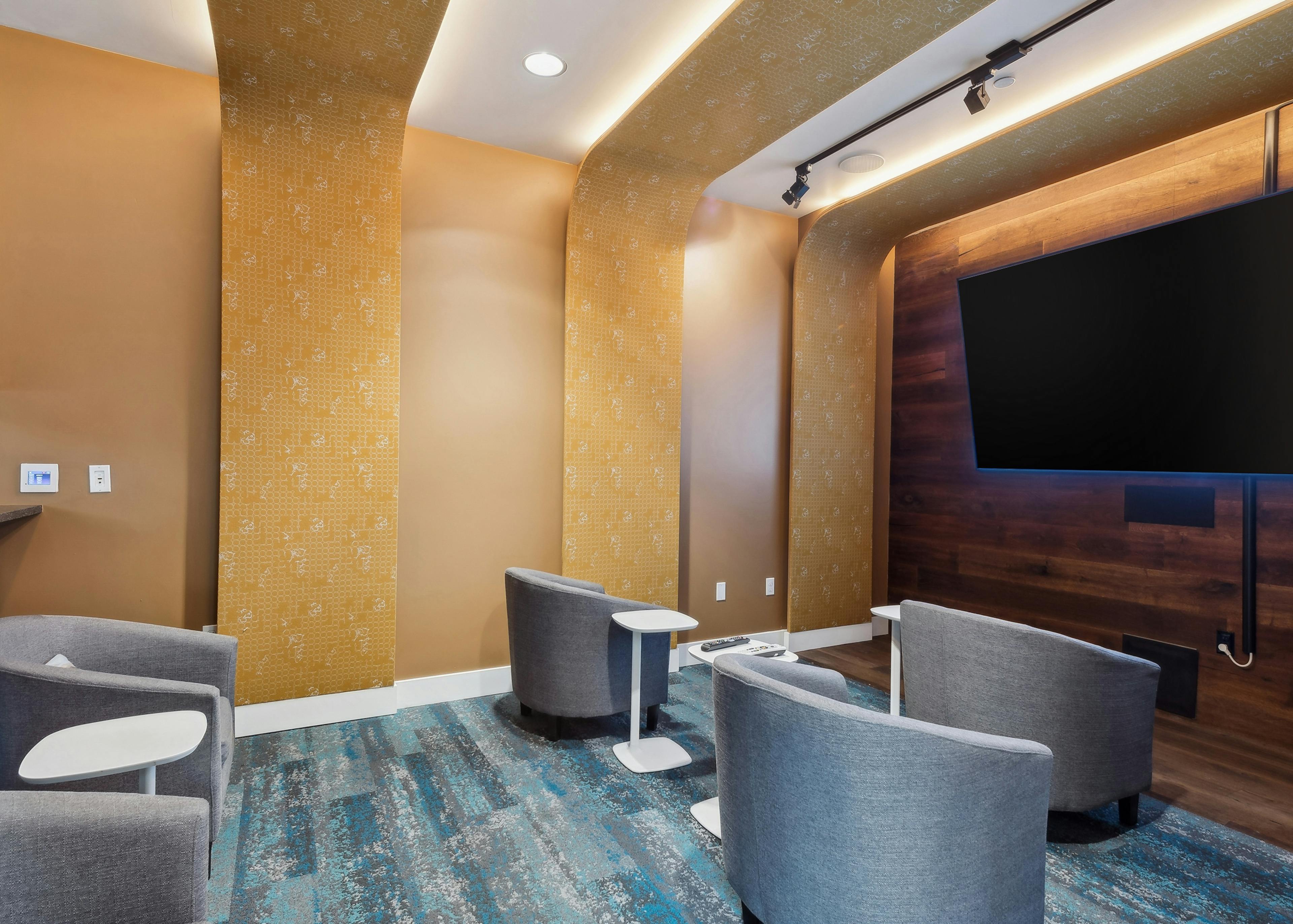 AMLI South Lake Union apartments resident movie theater with a large wall mounted TV and lounge chairs with side tables.