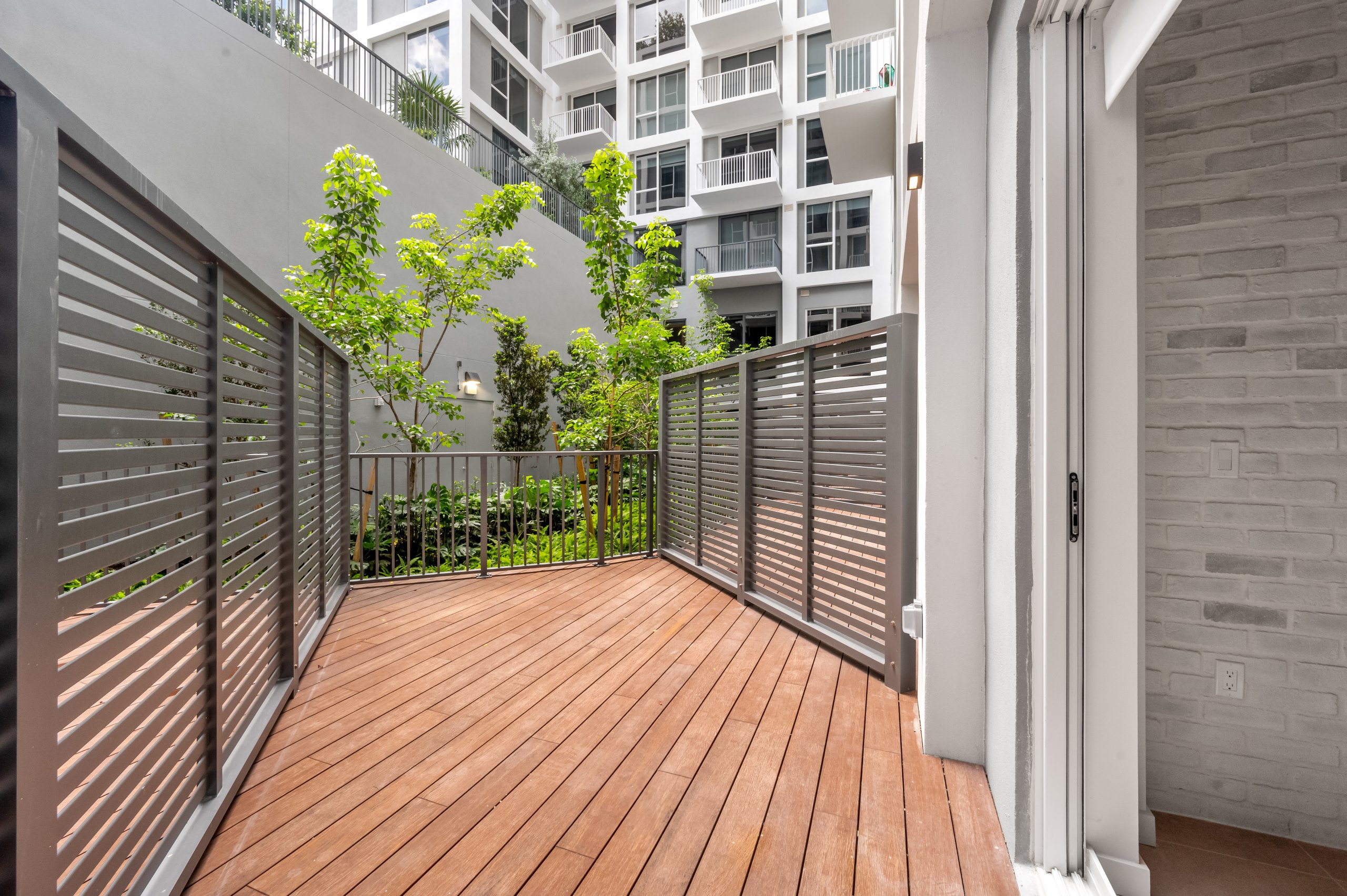 Exterior view of spacious private patio with wood decking and metal fencing overlooking greenery at AMLI Wynwood apartments.
