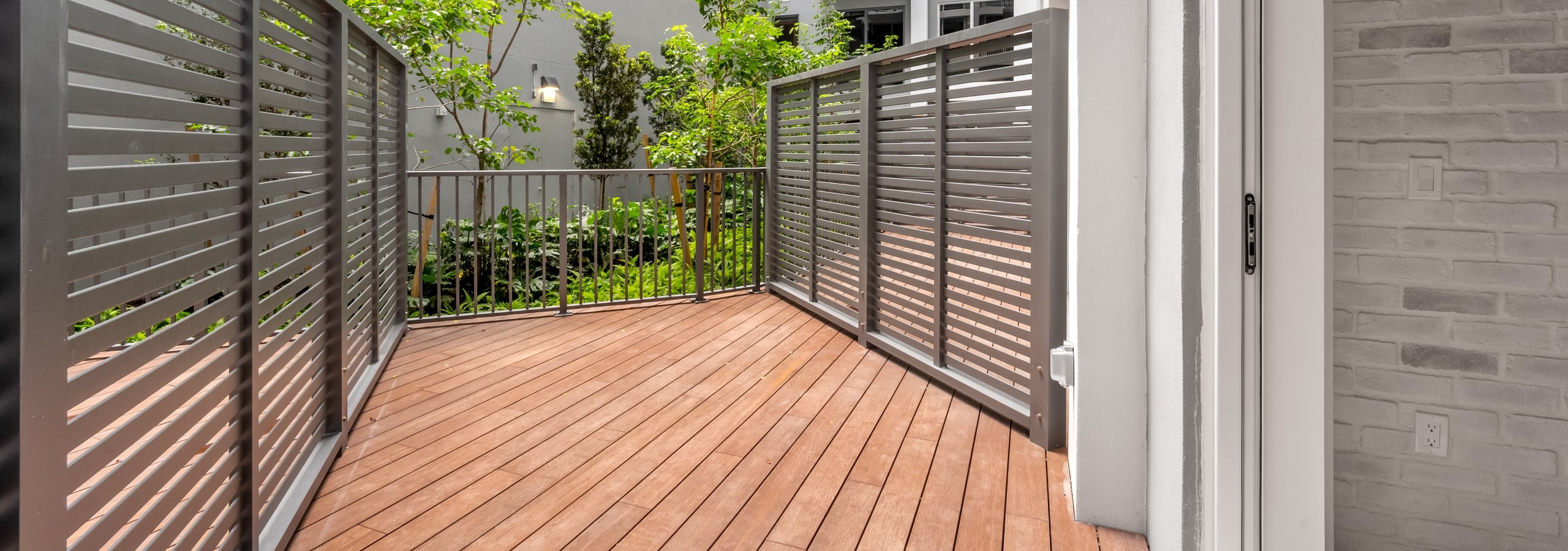 Exterior view of spacious private patio with wood decking and metal fencing overlooking greenery at AMLI Wynwood apartments.