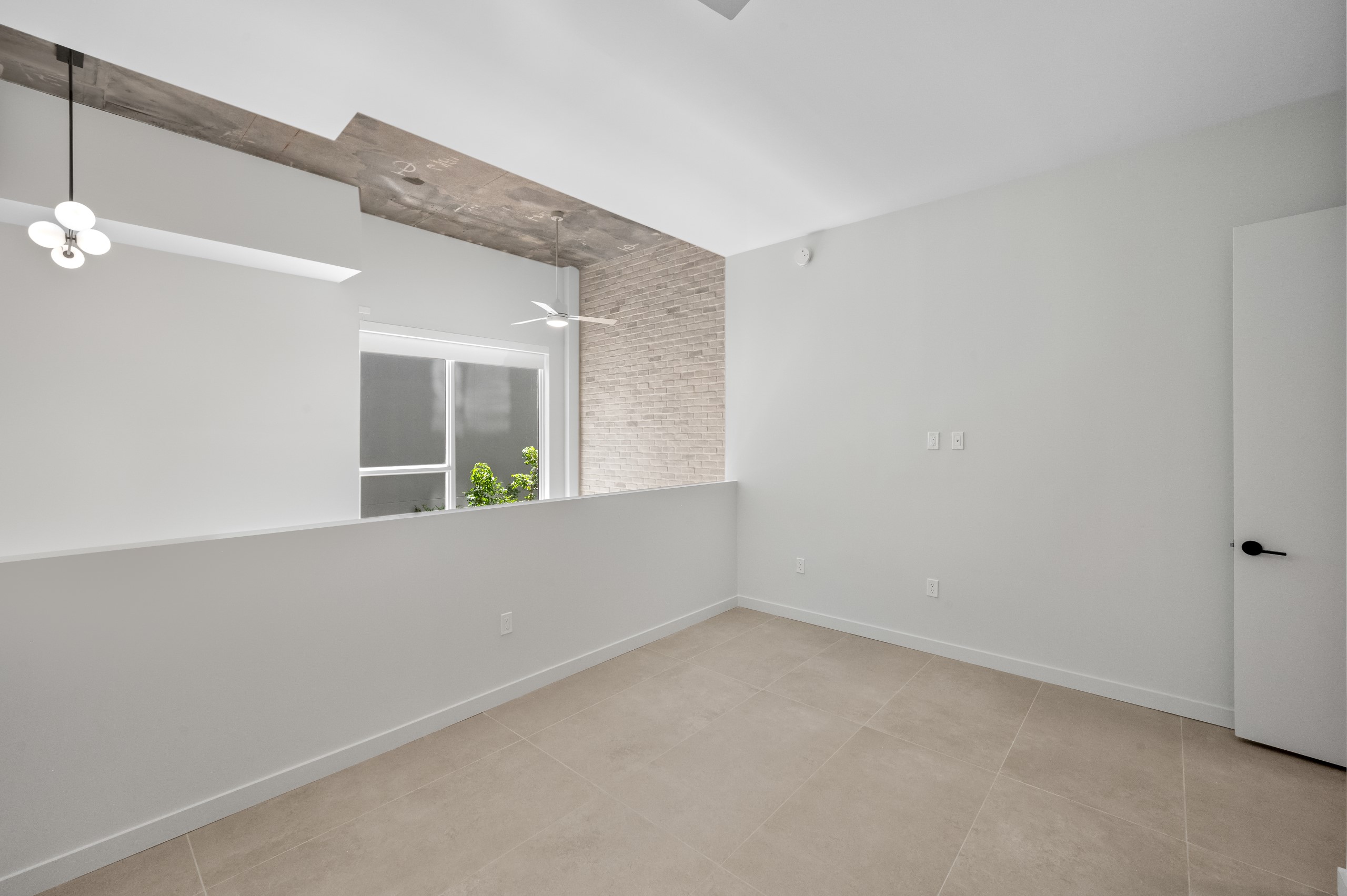 Interior view of loft area with exposed concrete ceiling, ceiling fan, modern lighting, and large window at AMLI Wynwood apartments.