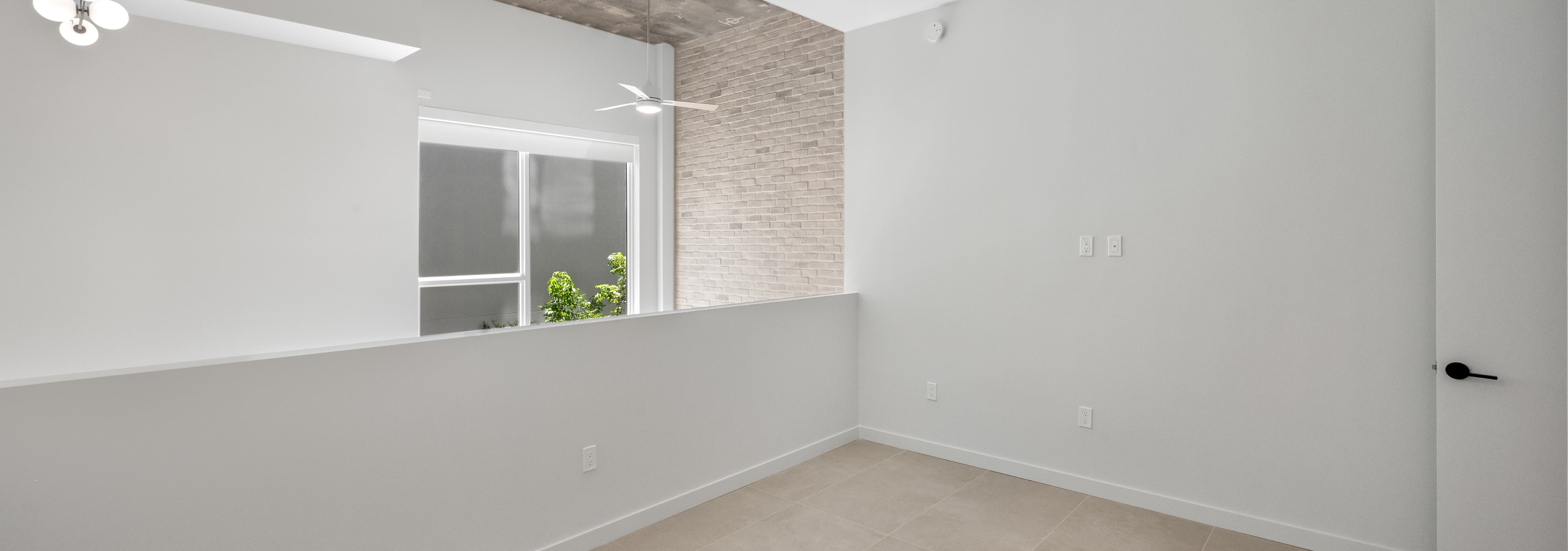 Interior view of loft area with exposed concrete ceiling, ceiling fan, modern lighting, and large window at AMLI Wynwood apartments.
