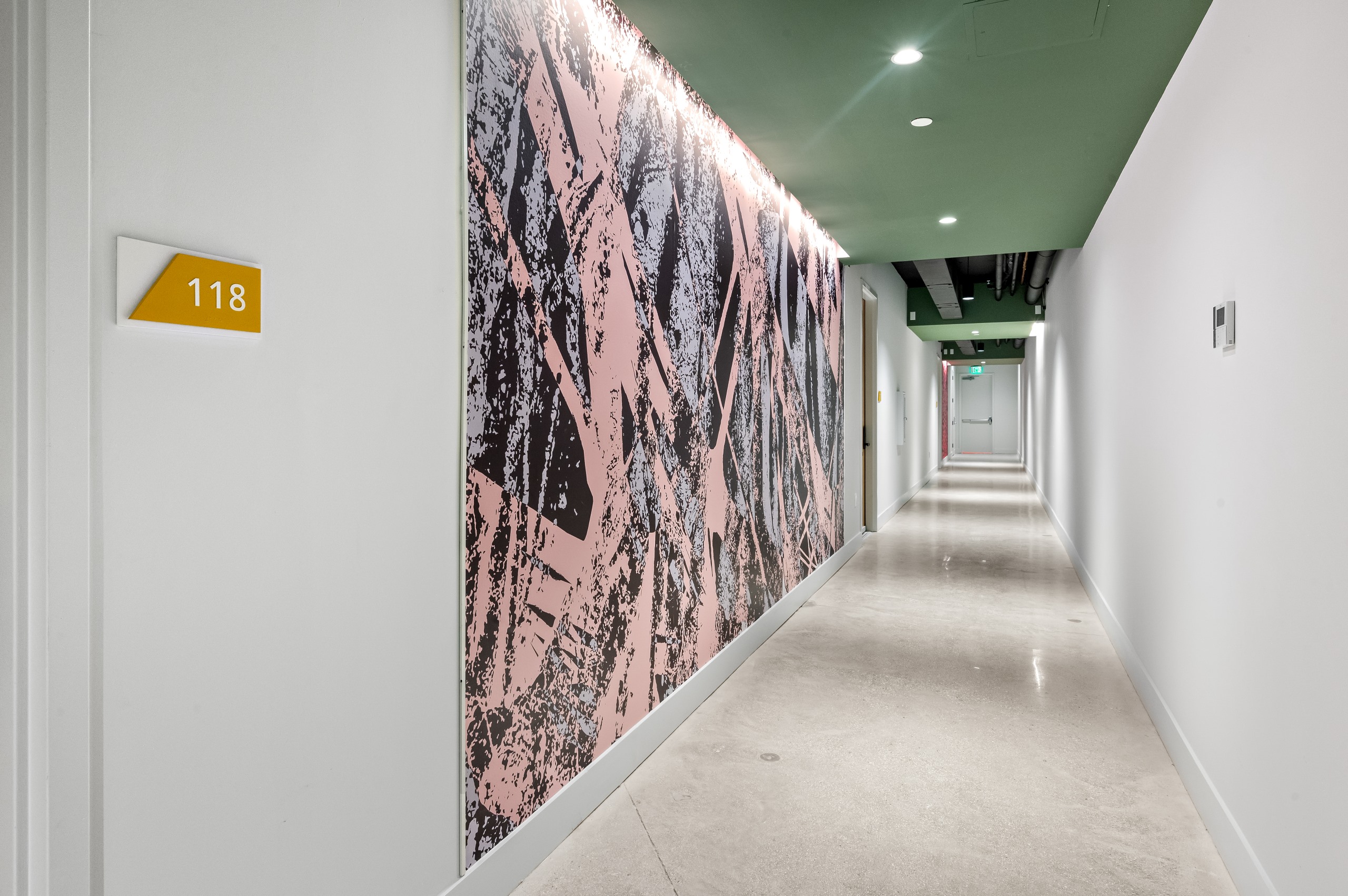 Interior view of long hallway with abstract wall mural and brightly polished concrete flooring at AMLI Wynwood apartments.