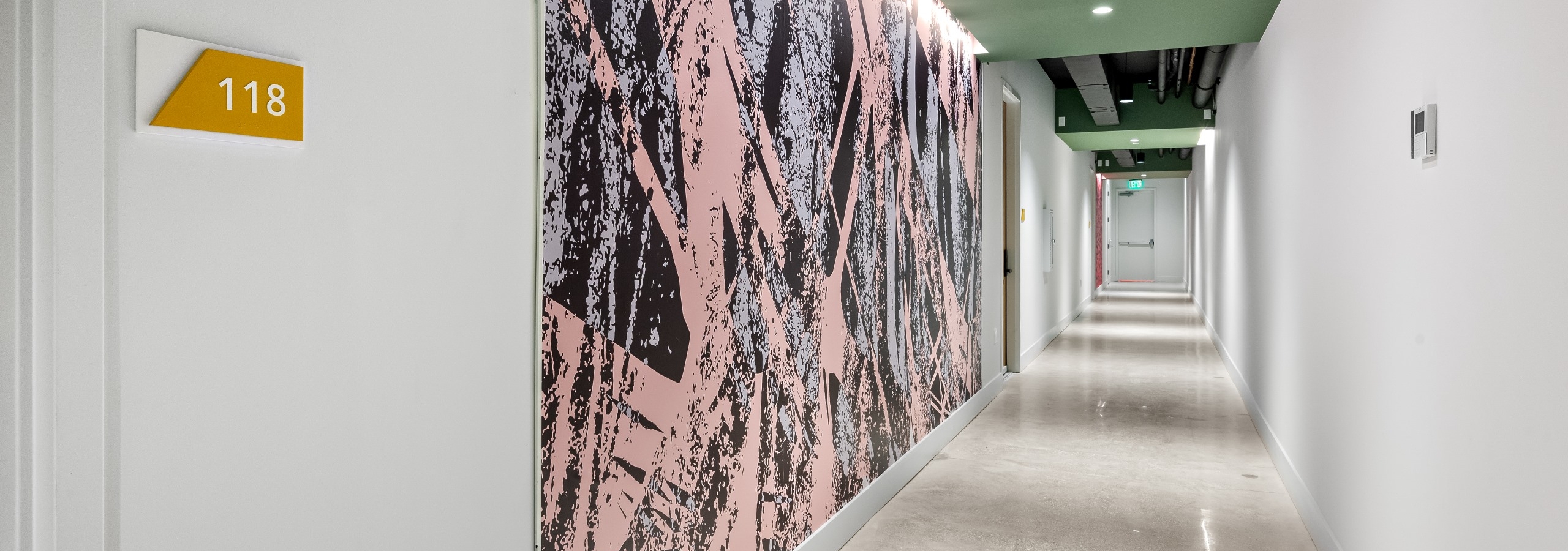Interior view of long hallway with abstract wall mural and brightly polished concrete flooring at AMLI Wynwood apartments.