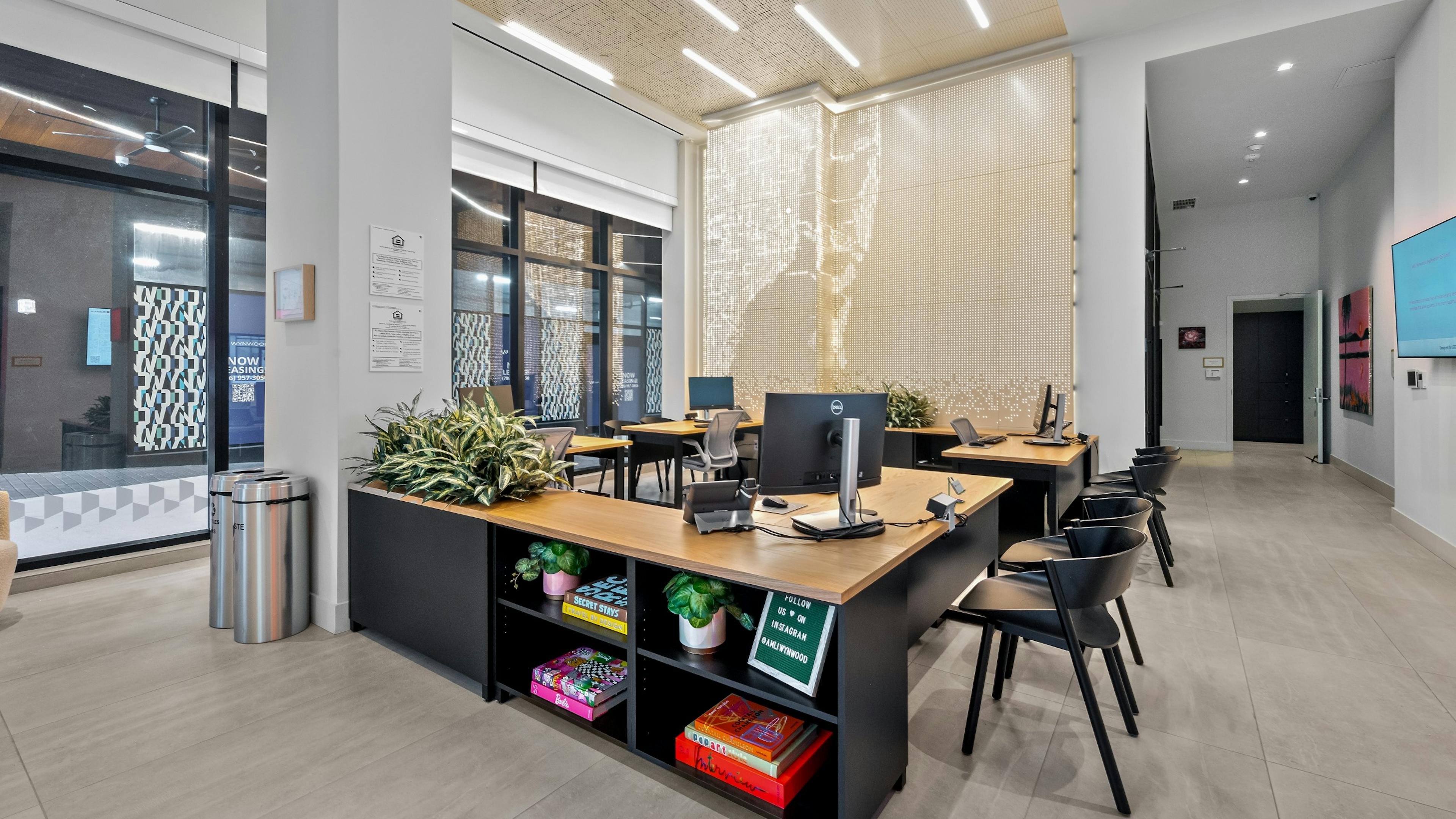AMLI Wynwood leasing office with black desks with light wood tops with computers and black chairs and a shimming wall and ceiling.