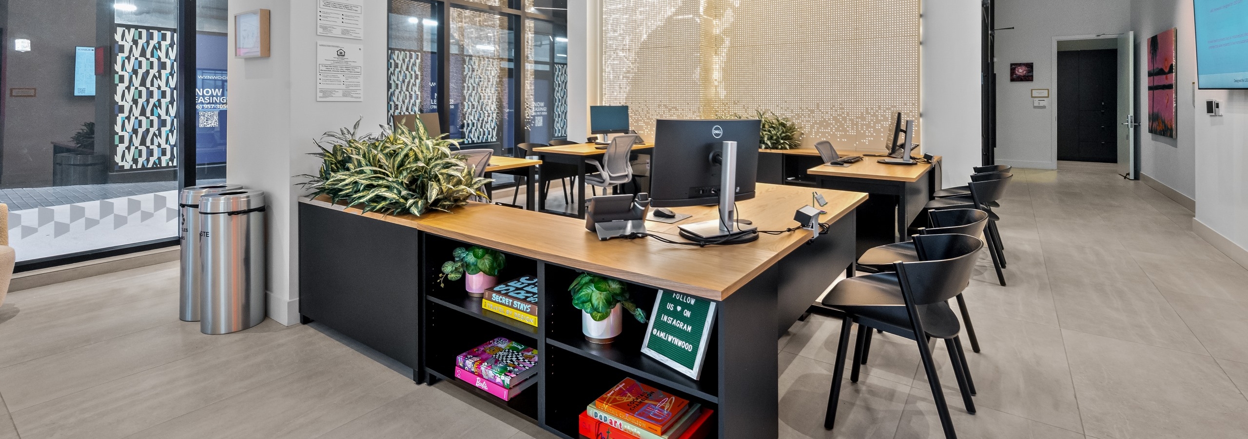 AMLI Wynwood leasing office with black desks with light wood tops with computers and black chairs and a shimming wall and ceiling.