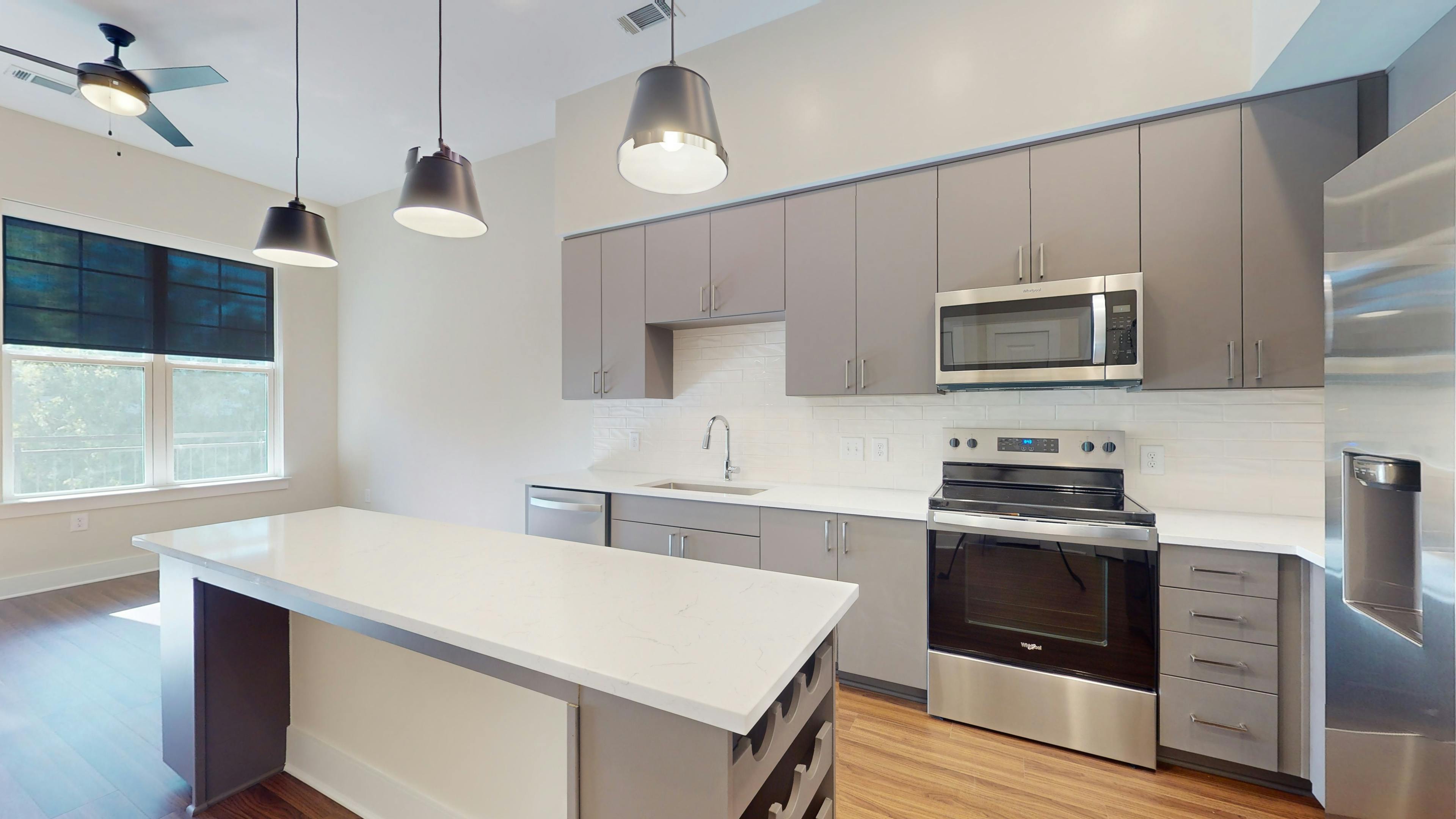 AMLI Brookhaven apartment kitchen with white counters, gray cabinets, a built in wine rack, wood floors and stainless steel appliances.