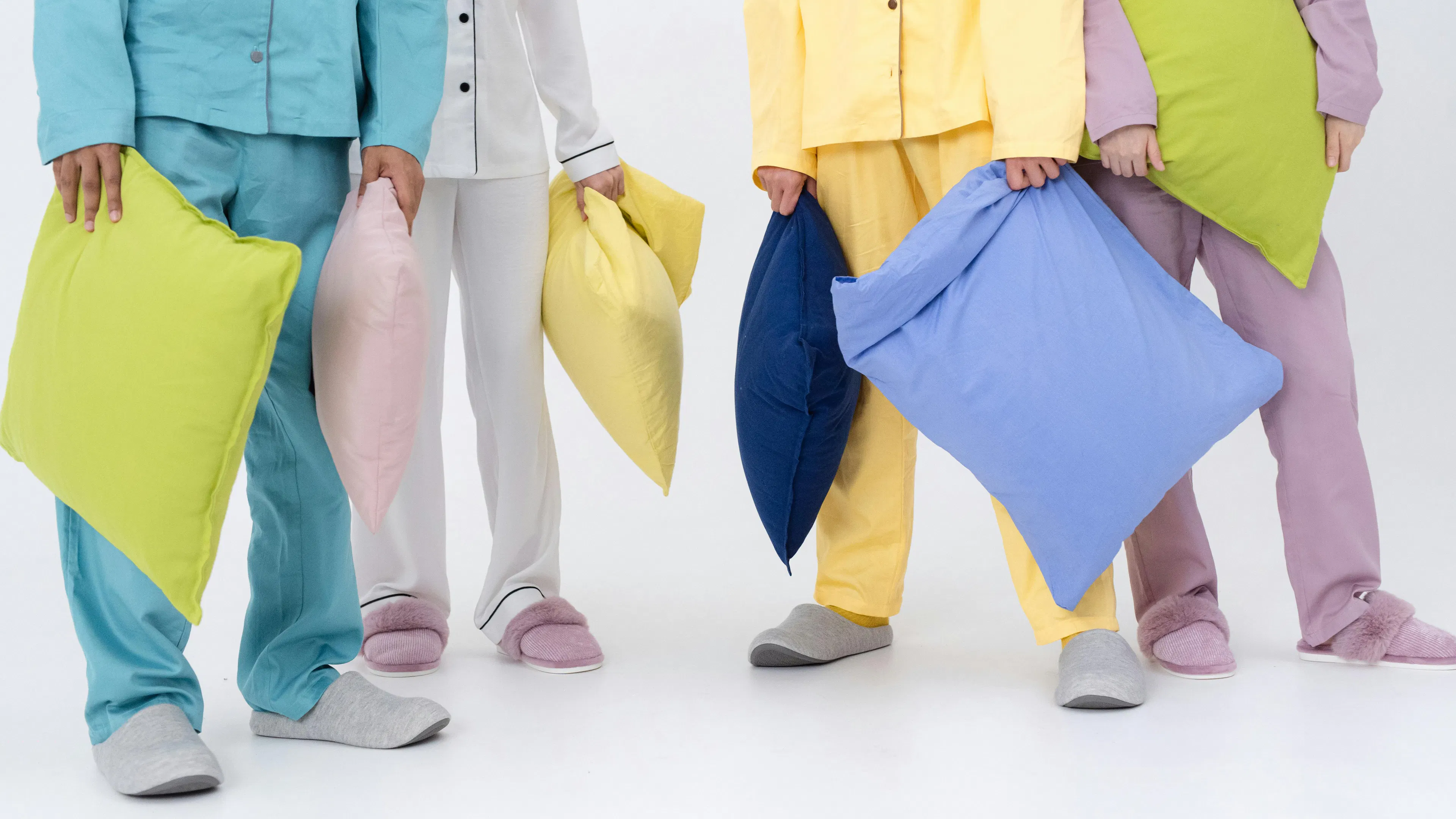 People from shoulders down in multi colored pajamas holding mulit colored pillows
