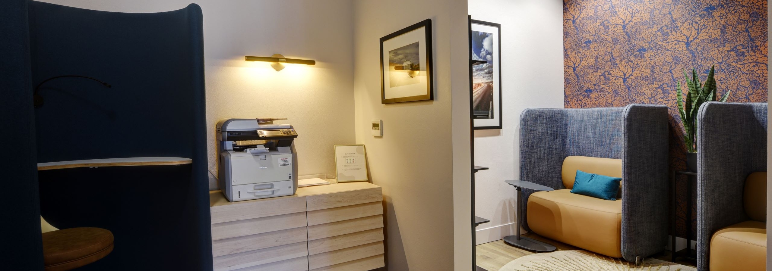Workstation at AMLI South Lake Union apartments with printer, framed artwork, and cozy seating alcoves featuring blue and tan booths.