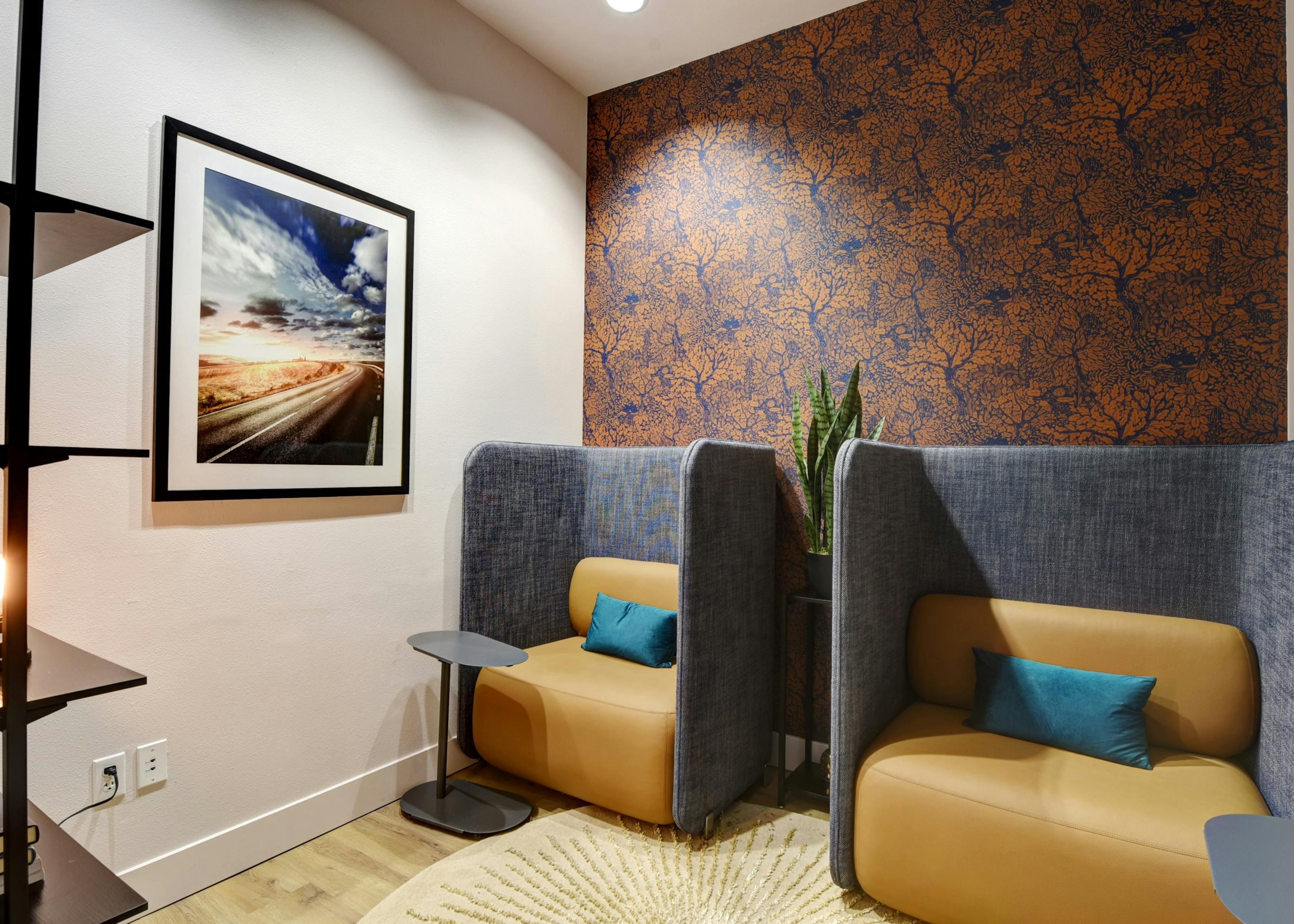 AMLI South Lake Union apartment lounge with private booth seating, orange and blue accent wallpaper, framed art and a potted plant.