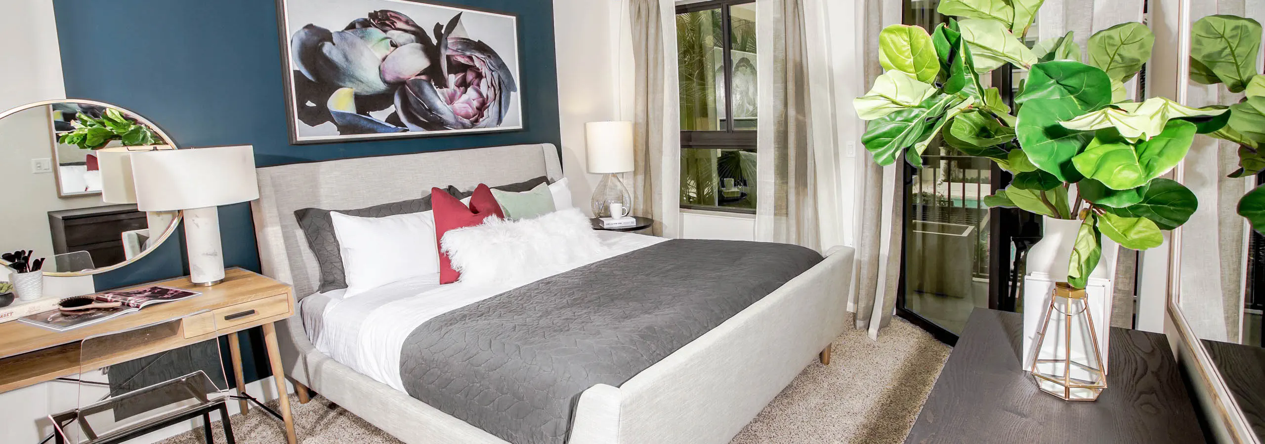 Interior view of an AMLI Joya apartment bedroom with a bed underneath black and white wall art and open window to a sky view.