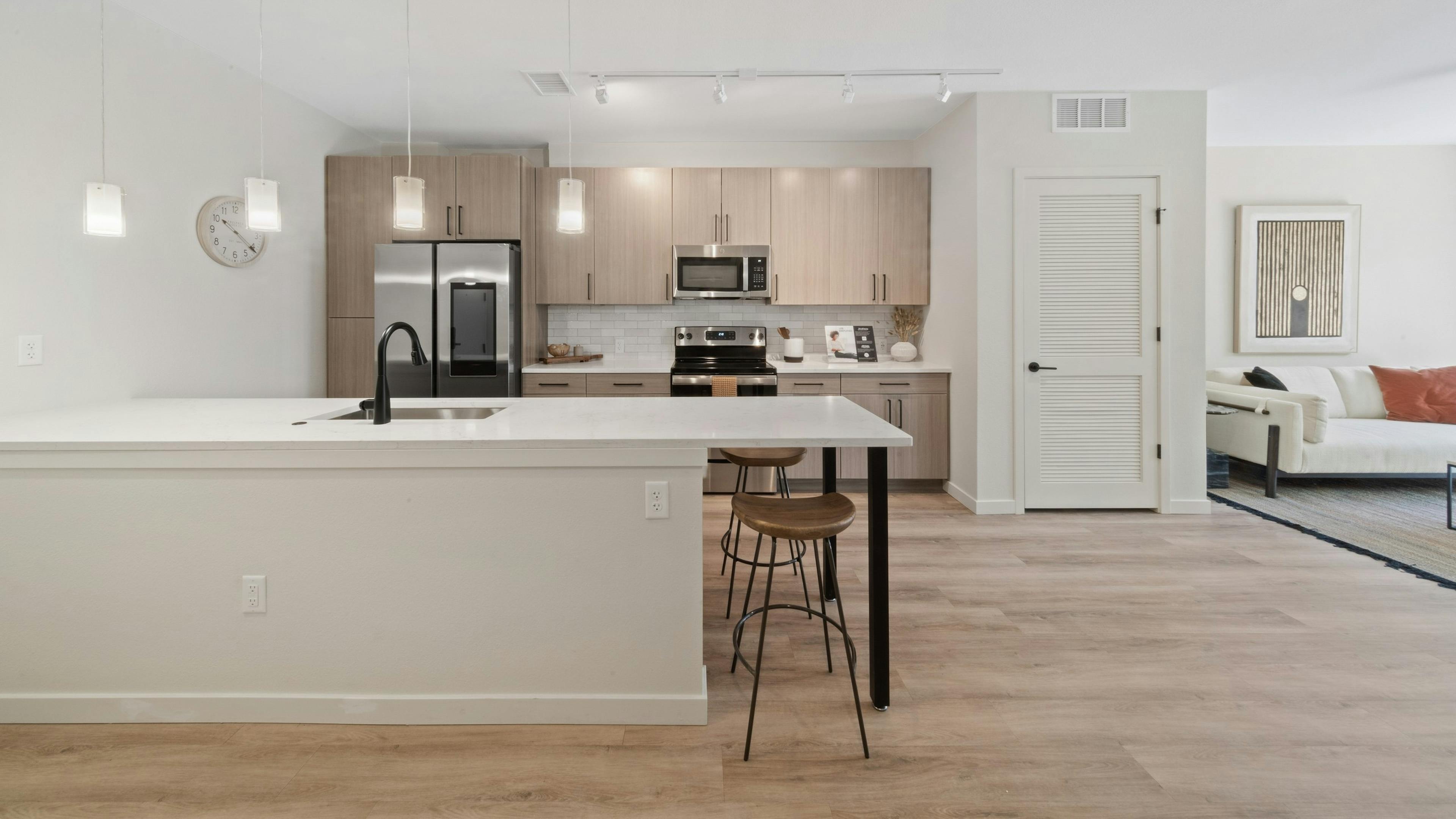 AMLI Broadway Park island kitchen featuring a stainless appliances and light wood grain cabinets over white tile backsplash 
